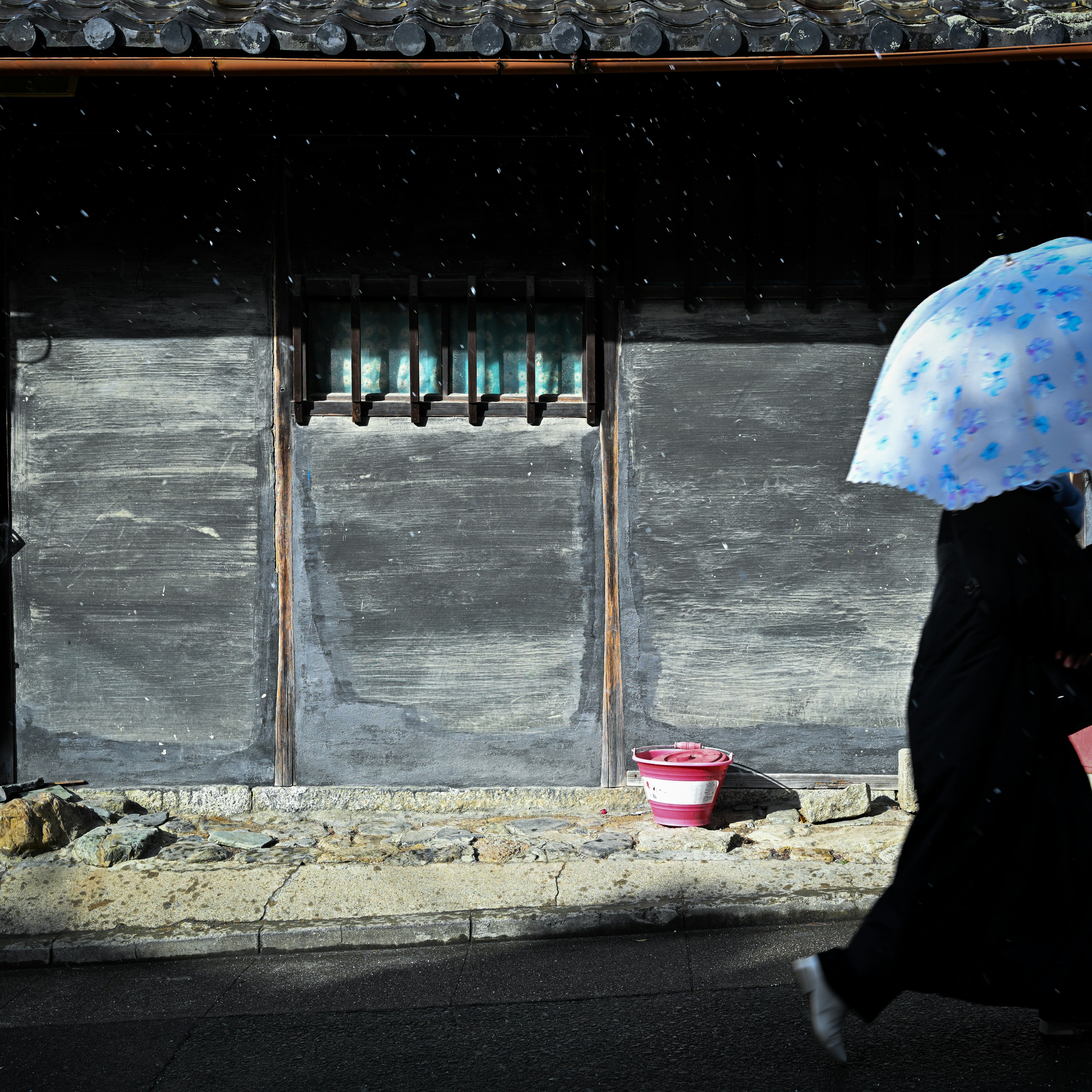 A person walking with an umbrella beside a traditional Korean house wall