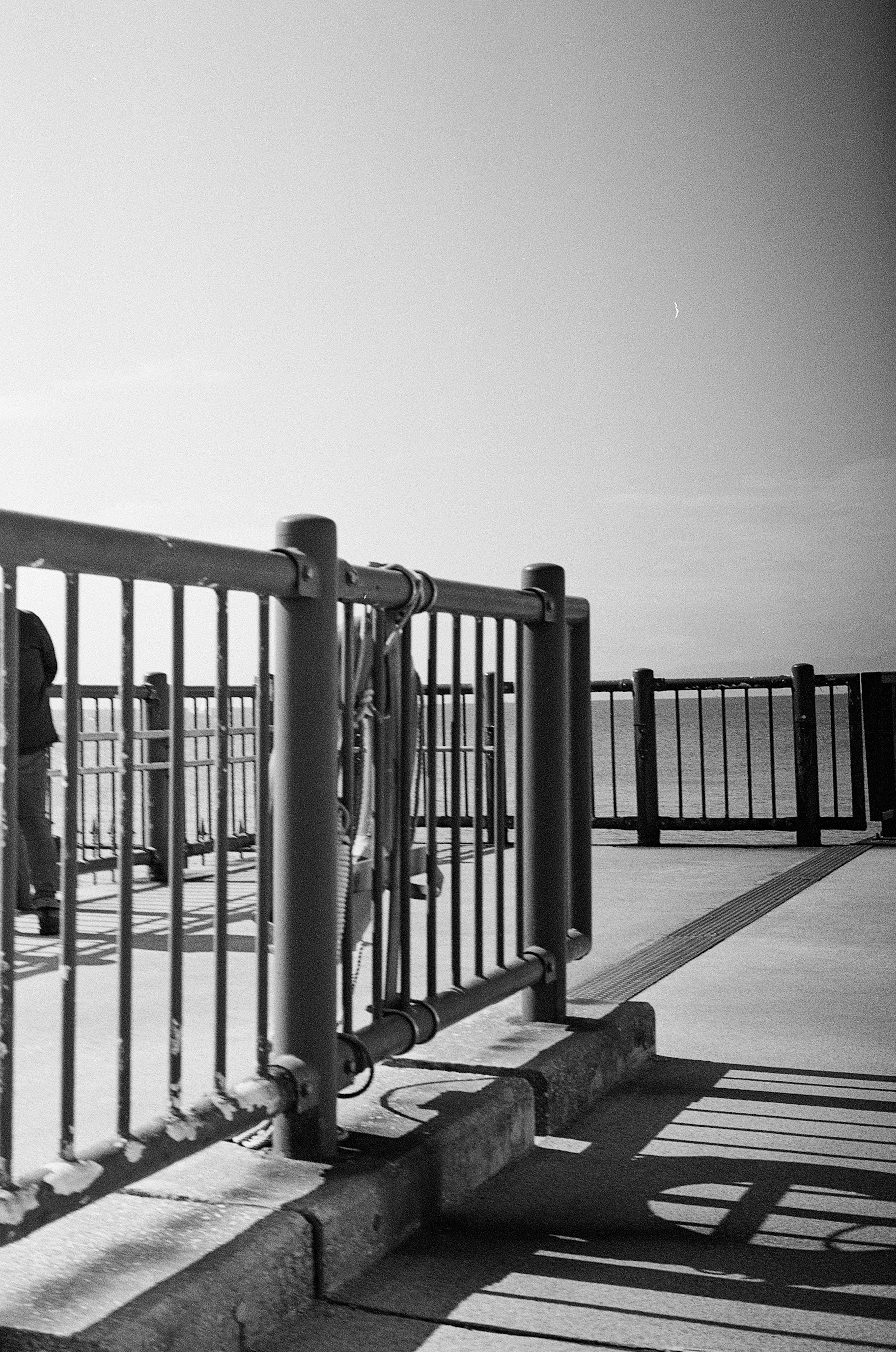 Black and white photo showing a section of a walkway with railings and distant figures