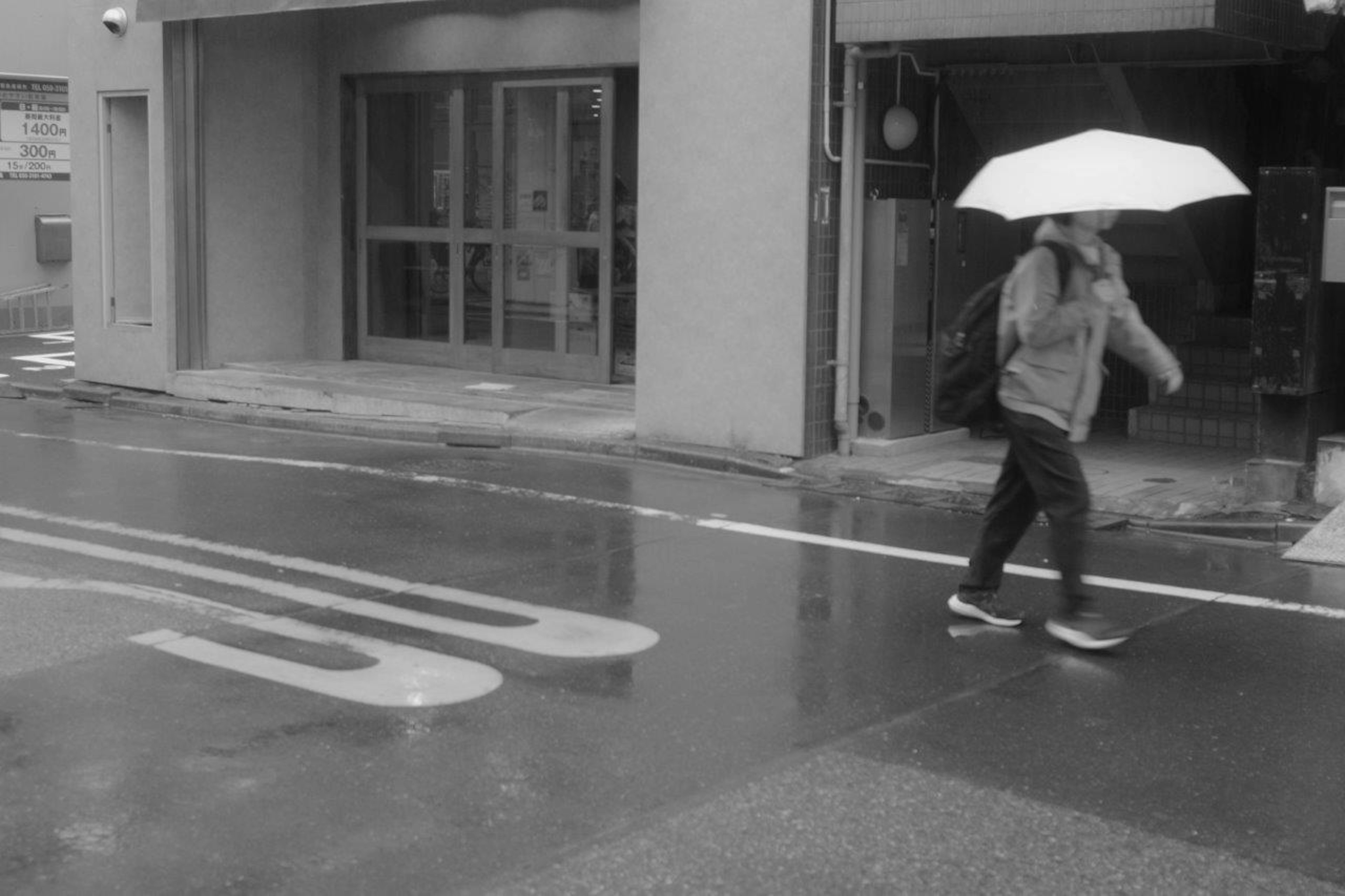 Black and white photo of a person walking with a white umbrella in the rain