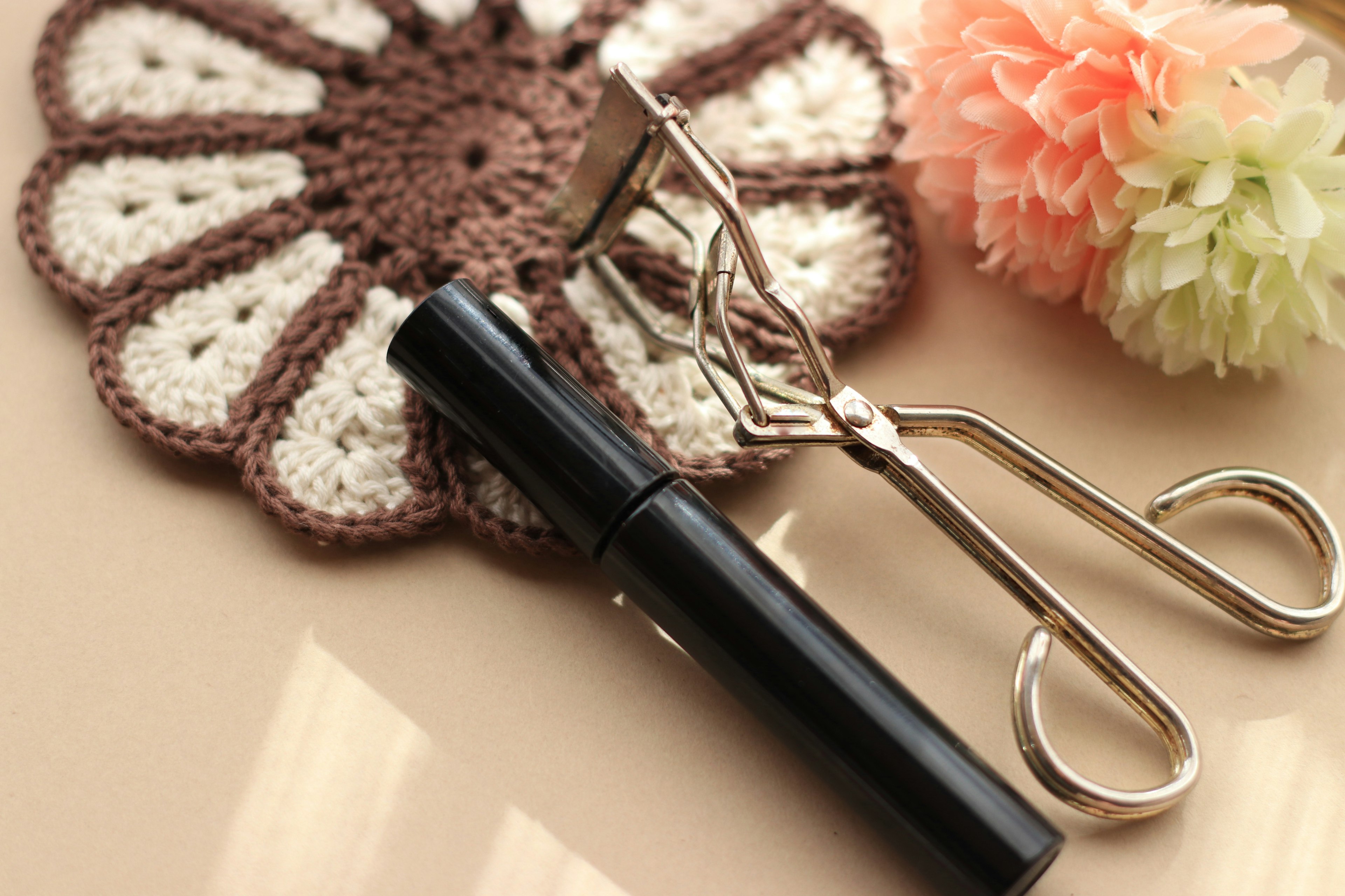 Black mascara and eyelash curler placed on a lace doily