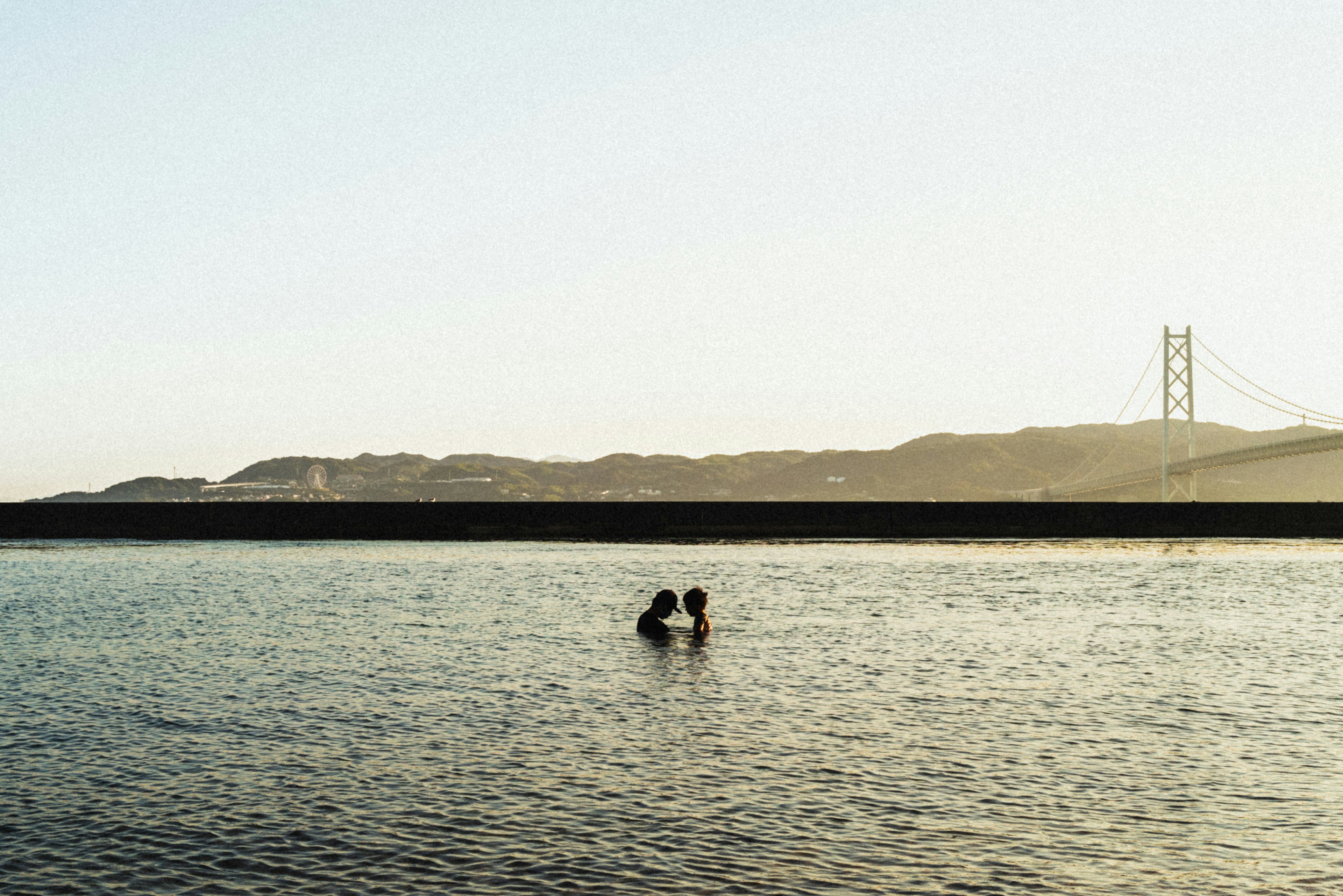 海で抱き合う二人のシルエットと橋の背景