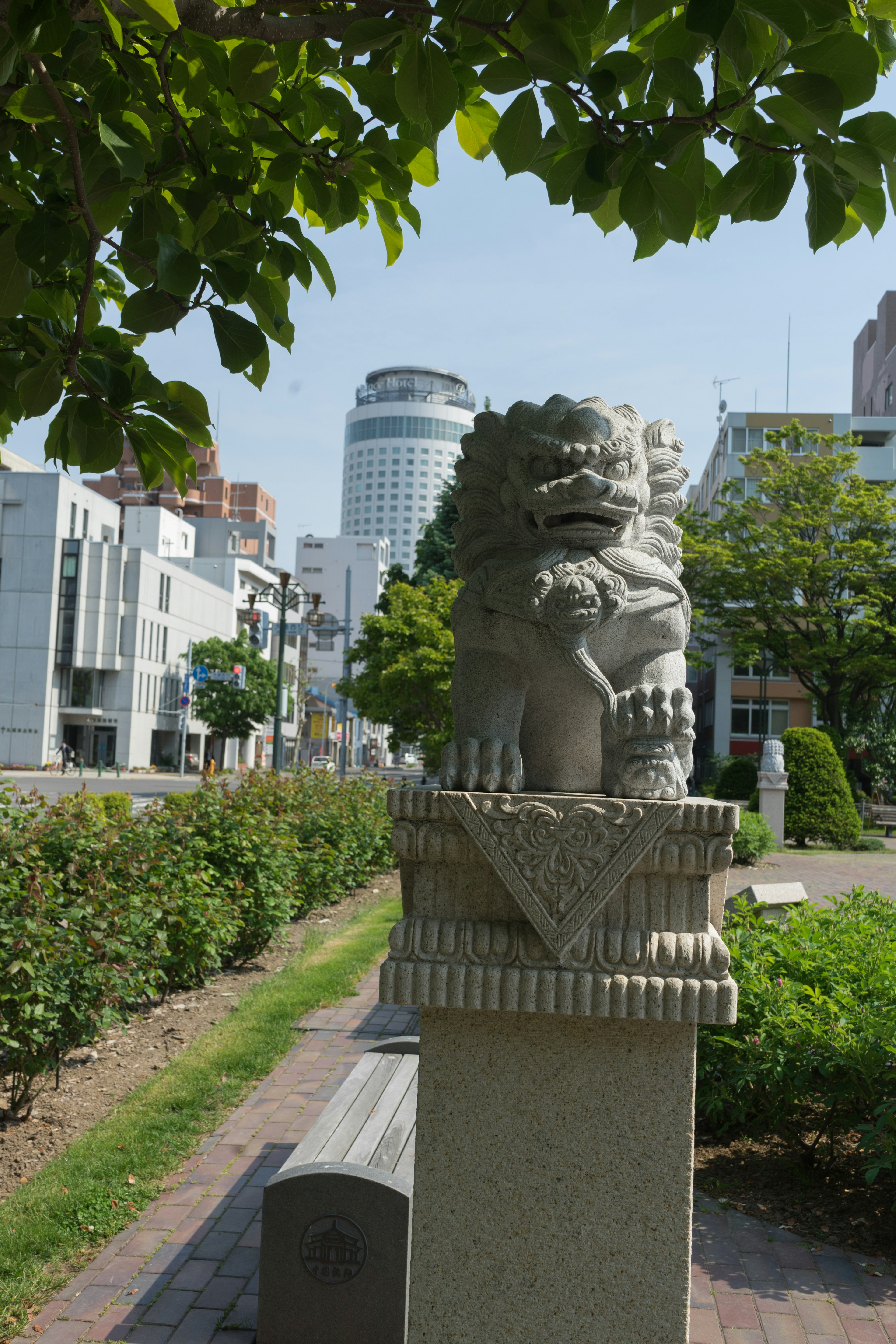 Statue de lion en pierre dans un parc avec des bâtiments modernes en arrière-plan