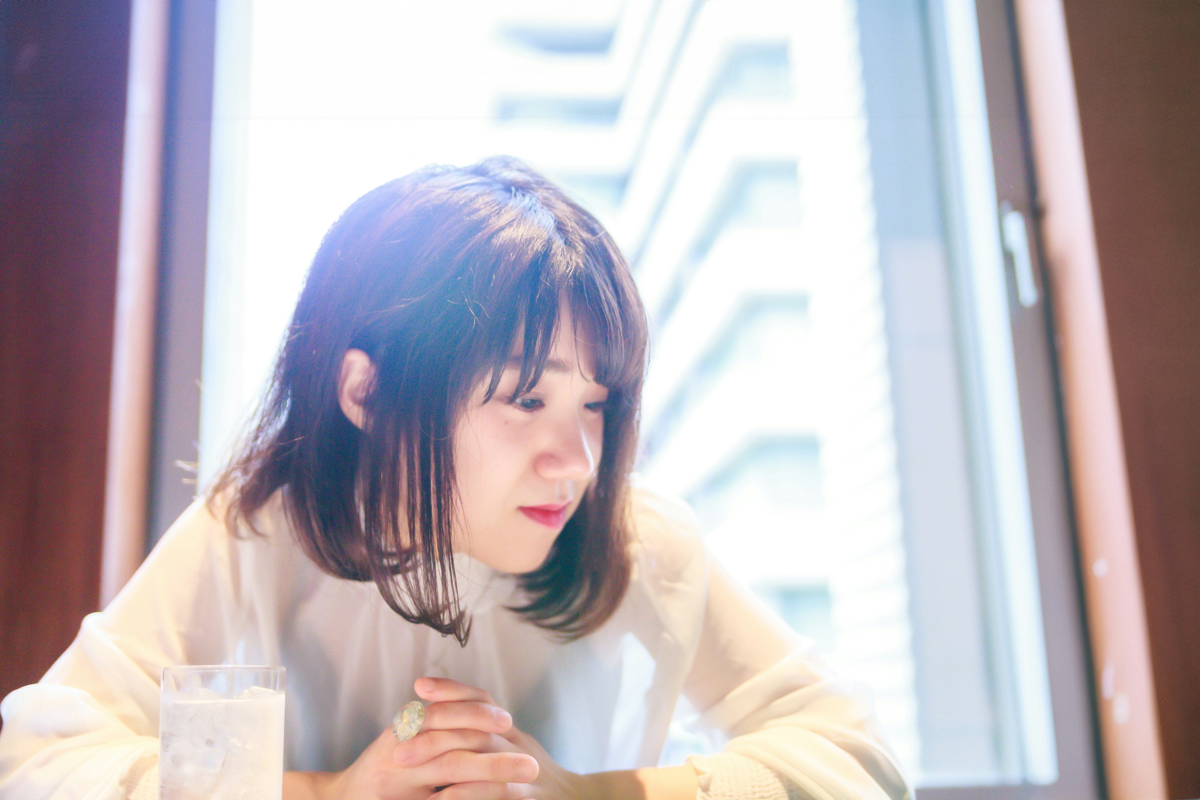 A woman deep in thought by the window wearing a white top