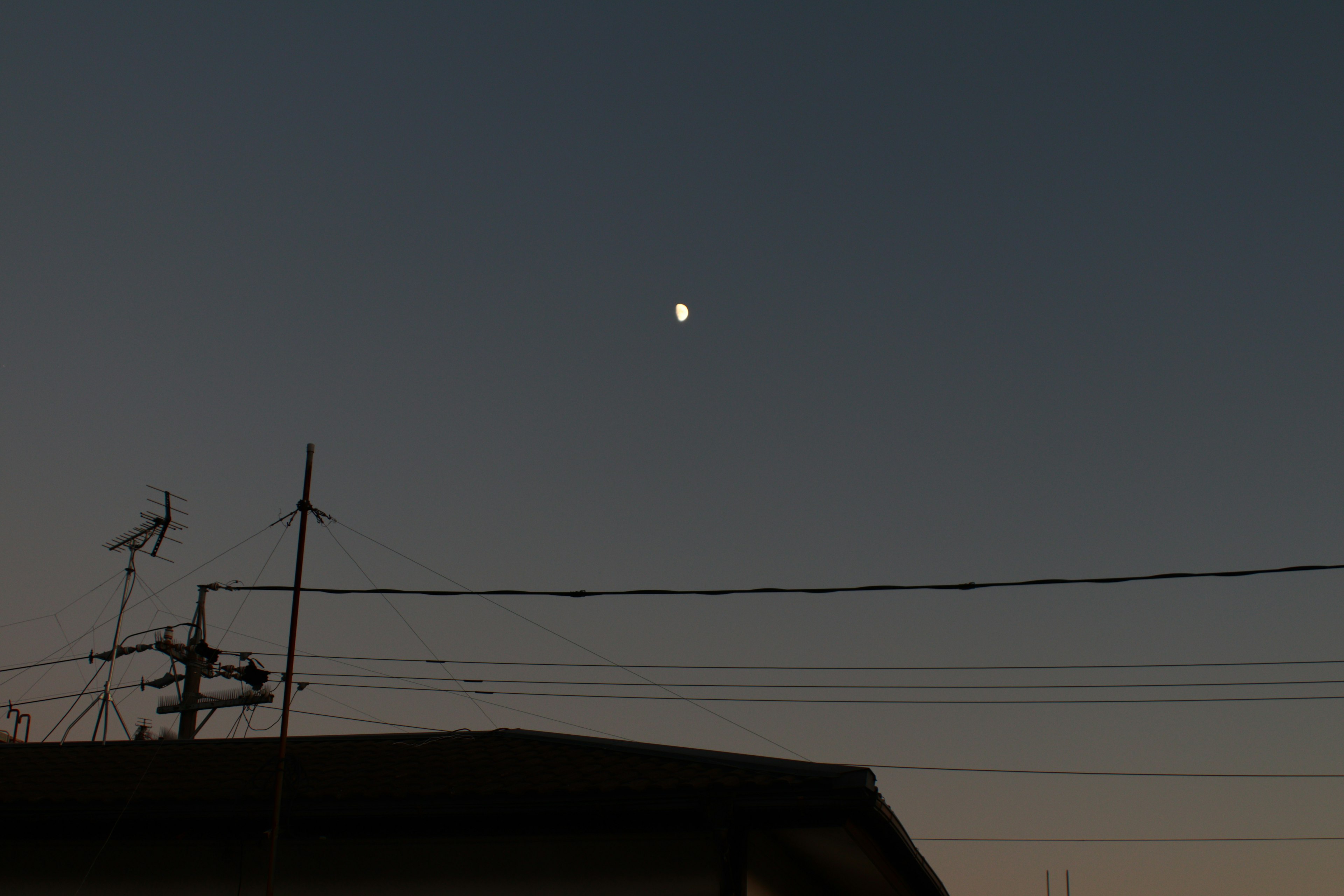 Luna en el cielo crepuscular con siluetas de líneas eléctricas