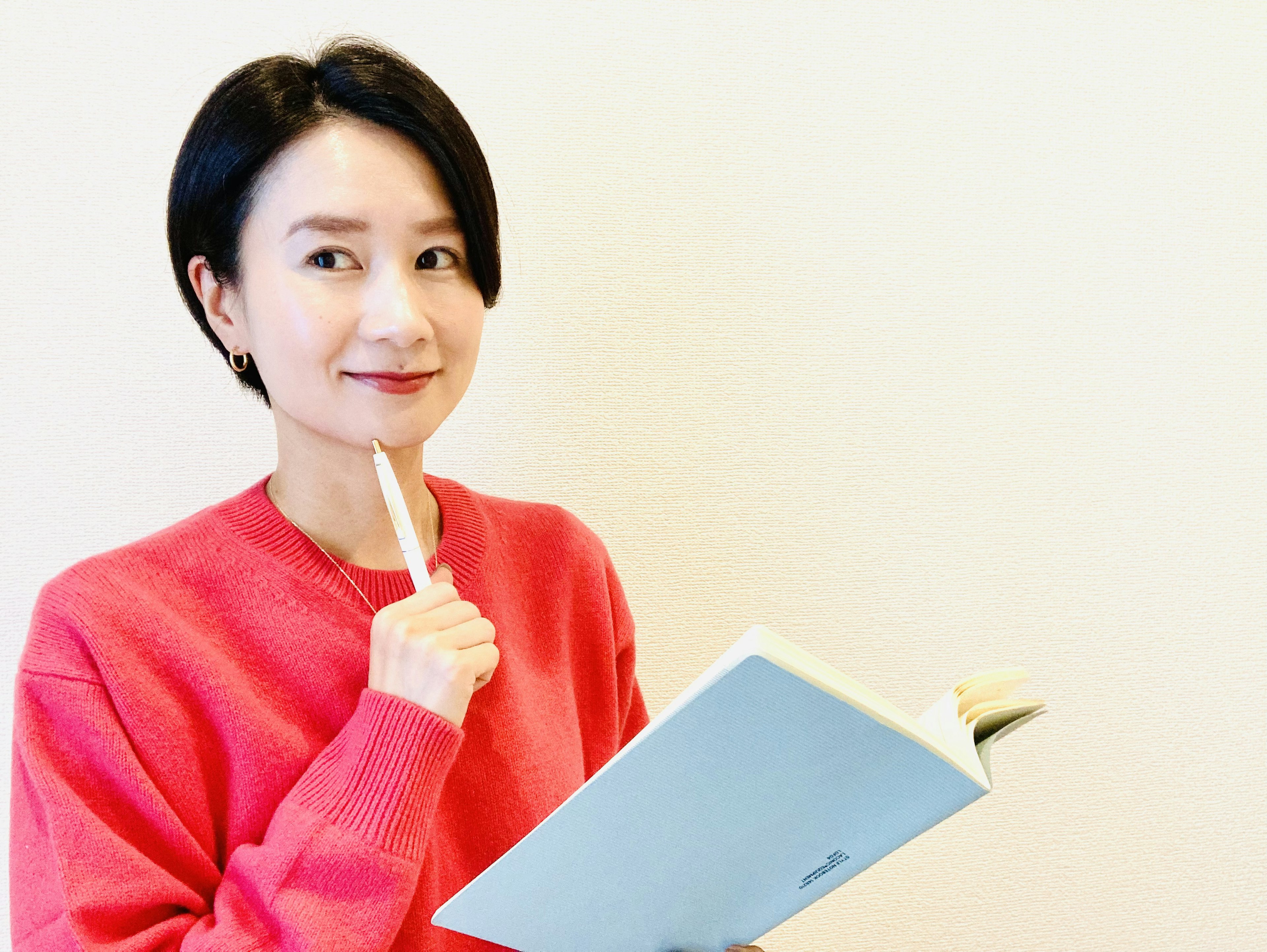 Young woman in a red sweater holding a notebook while thinking