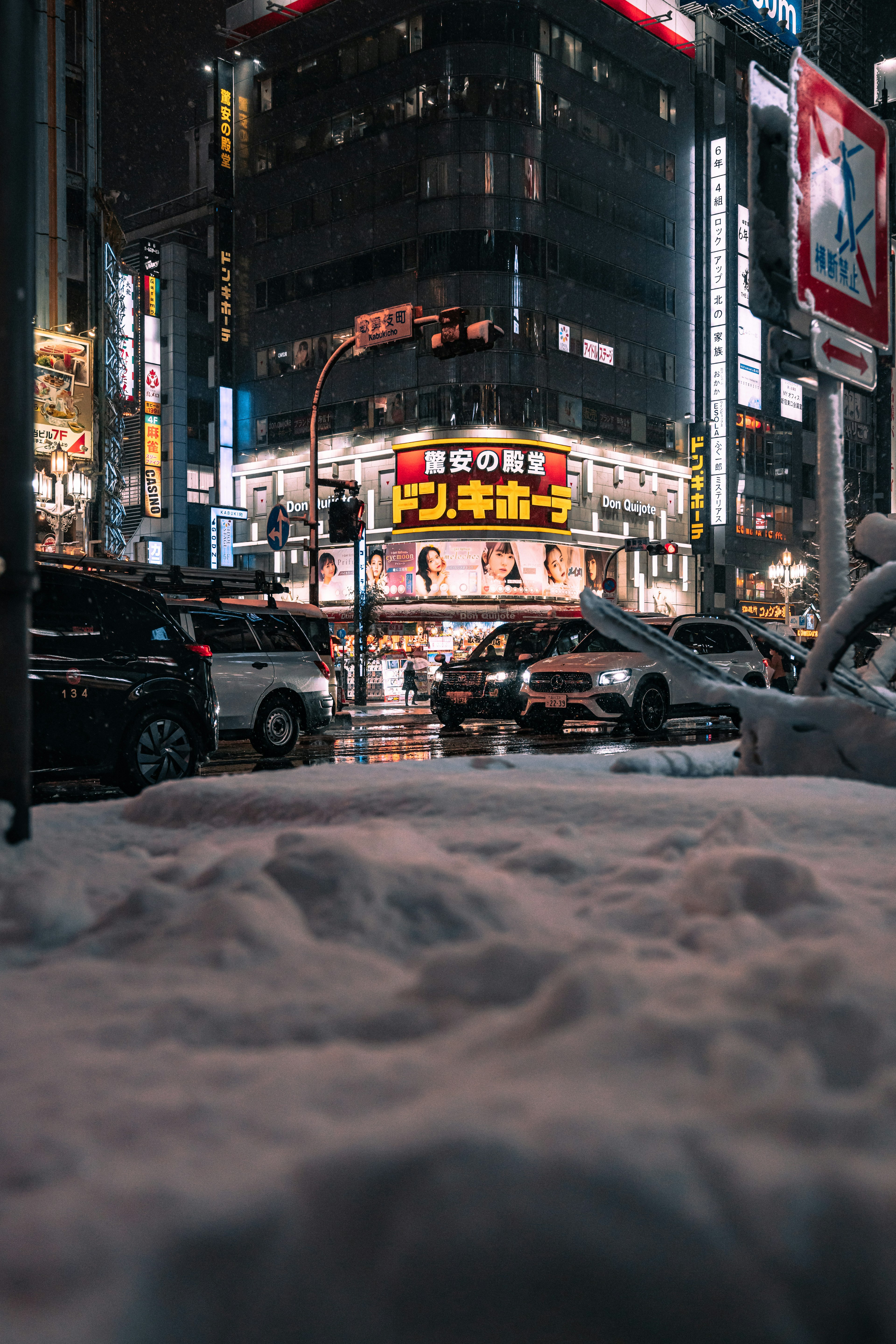 Schneebedeckter Straßenwinkel bei Nacht mit leuchtenden Neonzeichen und Autos