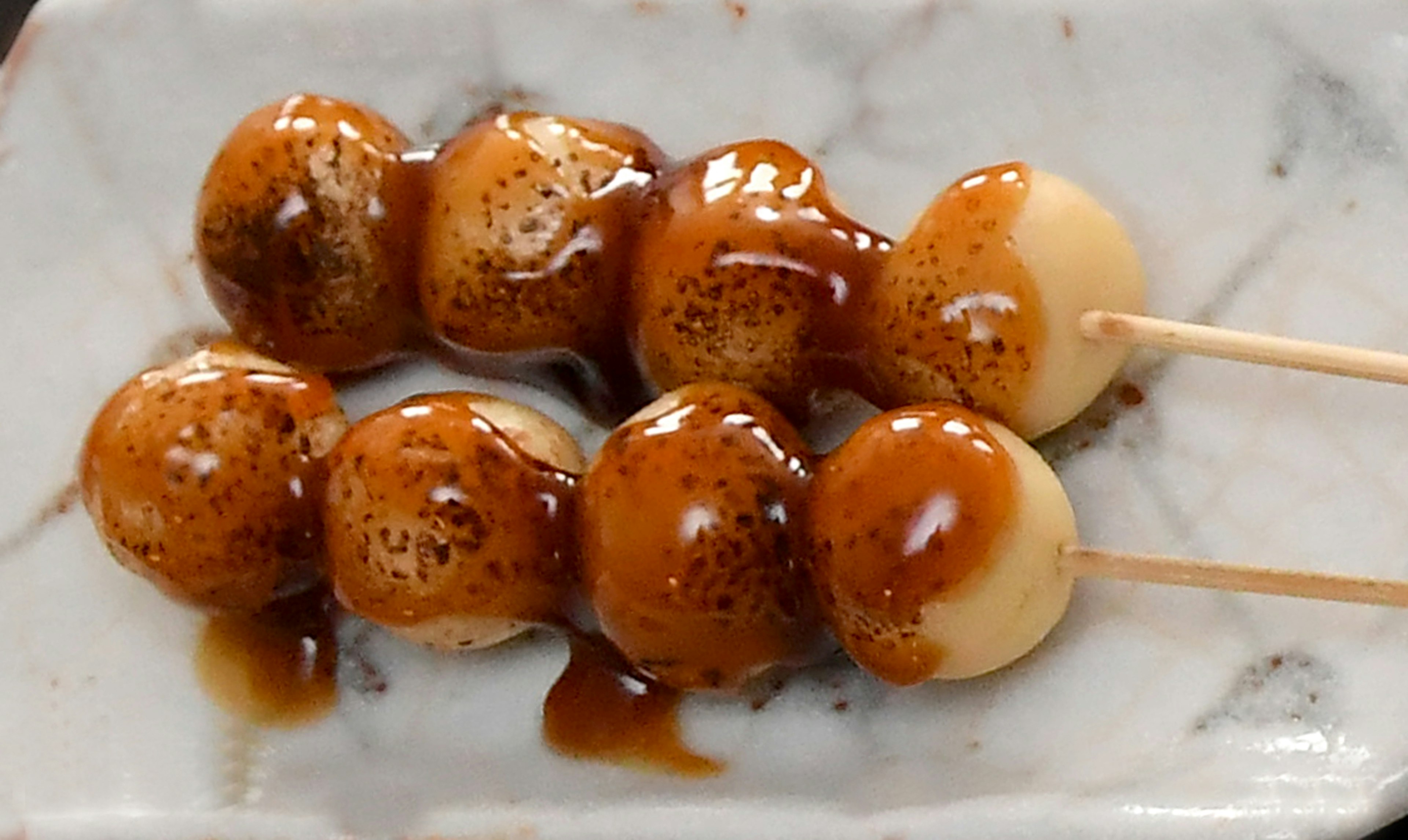 Tusuk Mitarashi dango disiram saus kedelai manis disajikan di atas piring