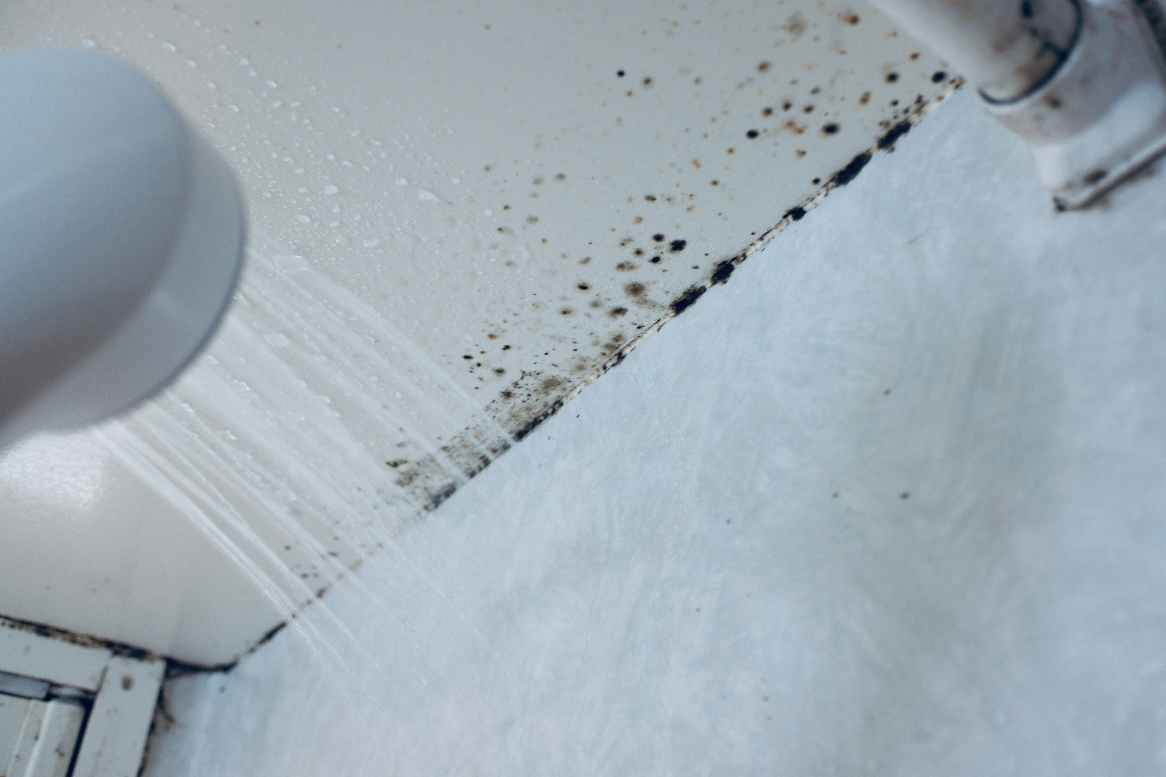 Agua fluyendo sobre una superficie blanca con moho en la pared