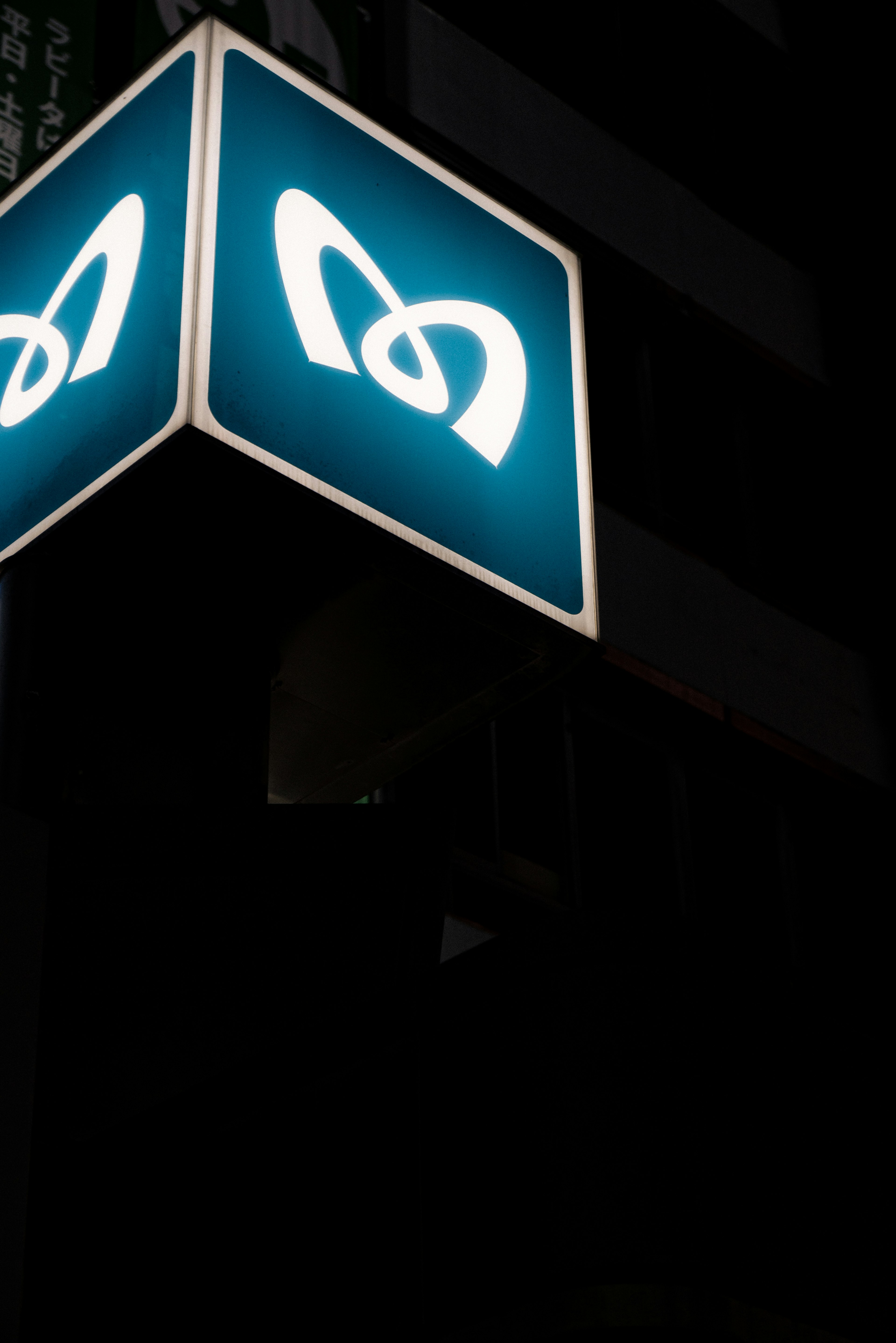 Illuminated sign with a blue background and white logo at night