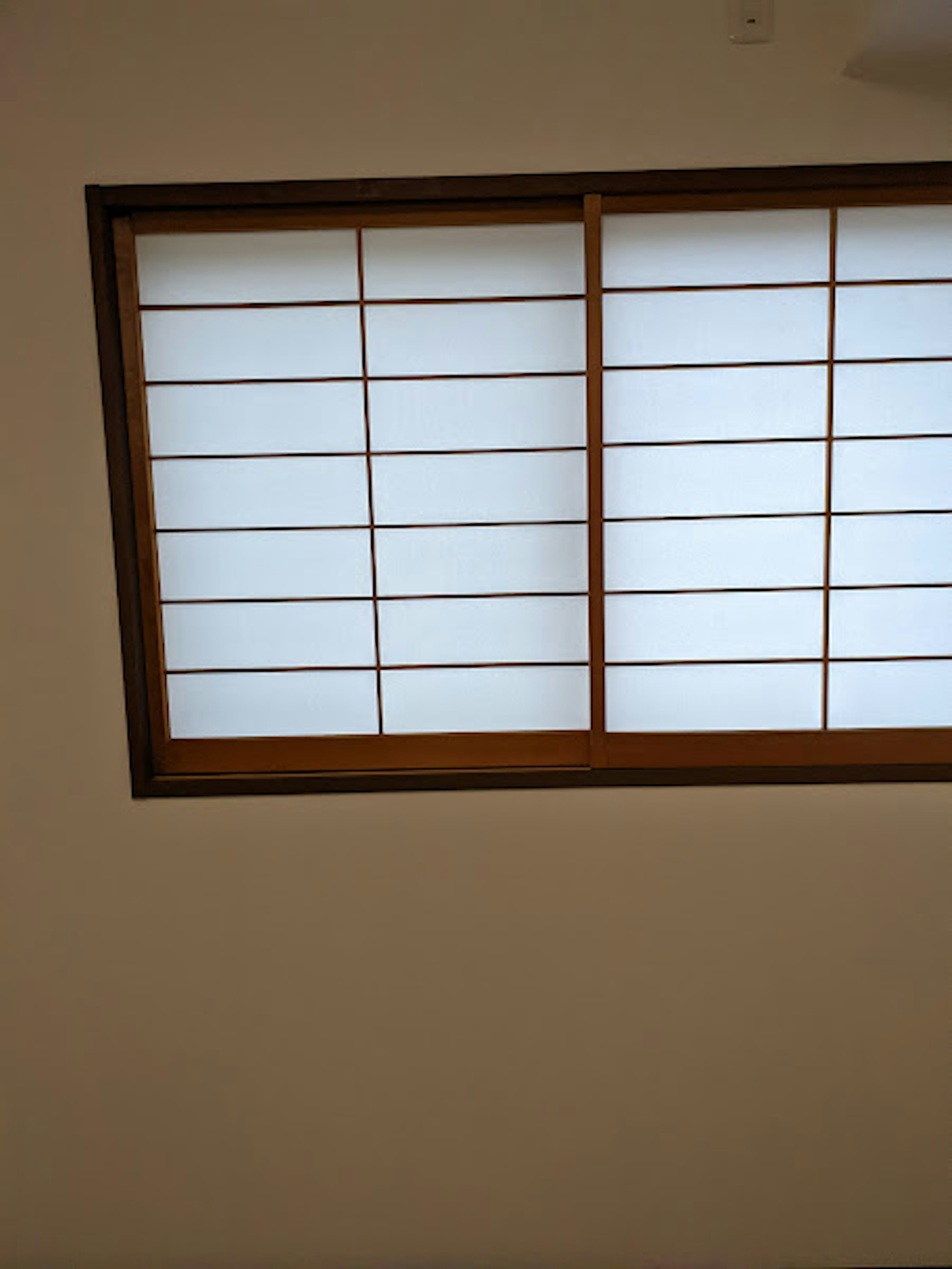 Wooden window with grid blinds on a white wall