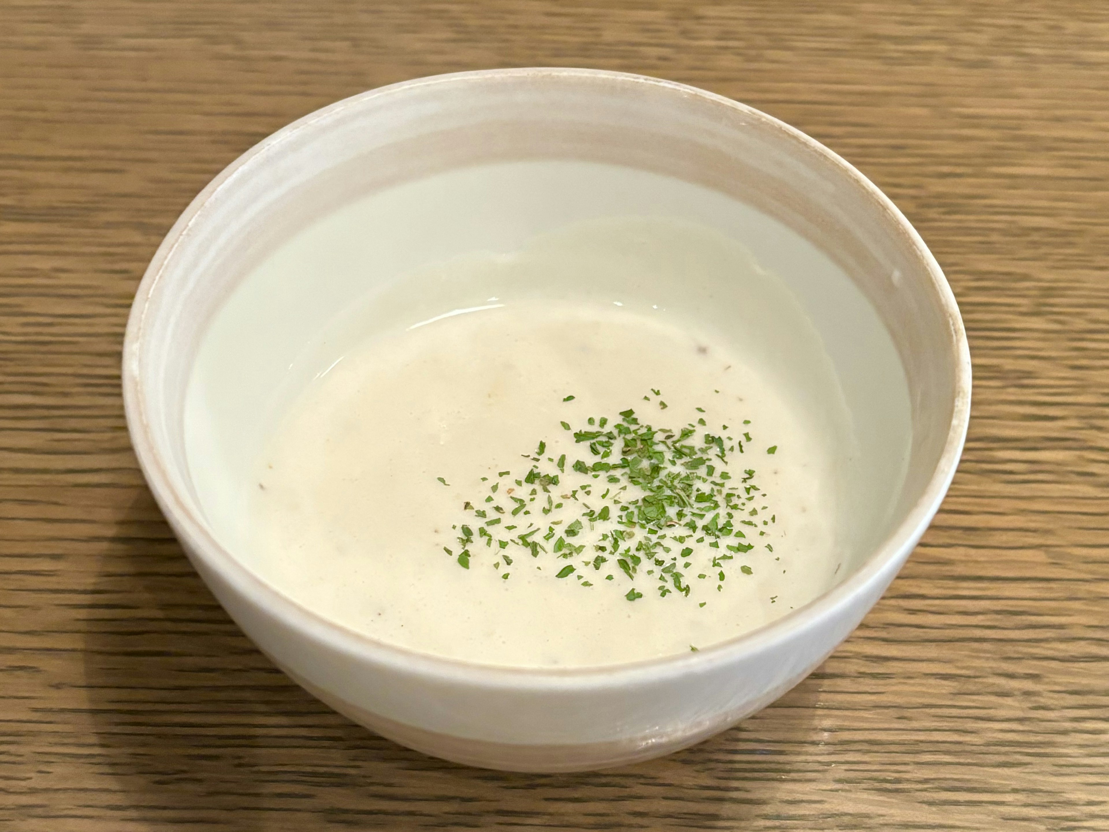 A bowl of white soup with green toppings sprinkled on top