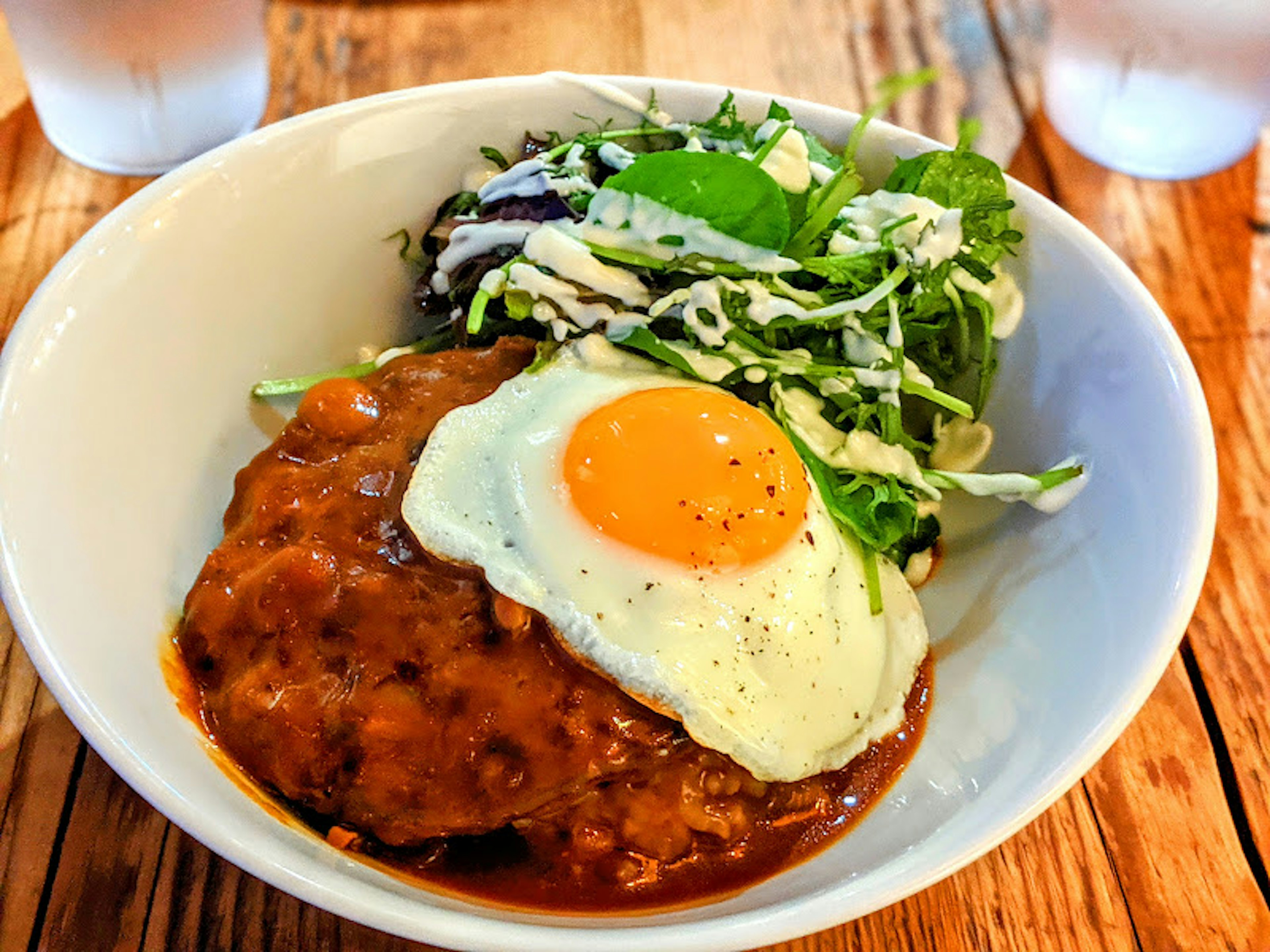 Plato con salsa gravy cubierto con un huevo frito y una ensalada al lado