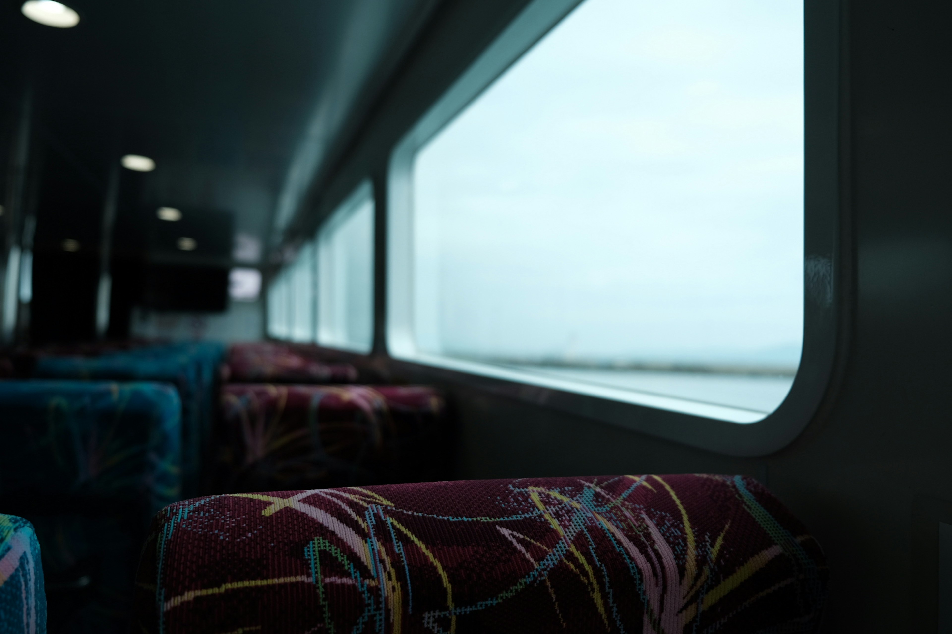 Interior view of a ferry with colorful patterned seats and cloudy sky outside