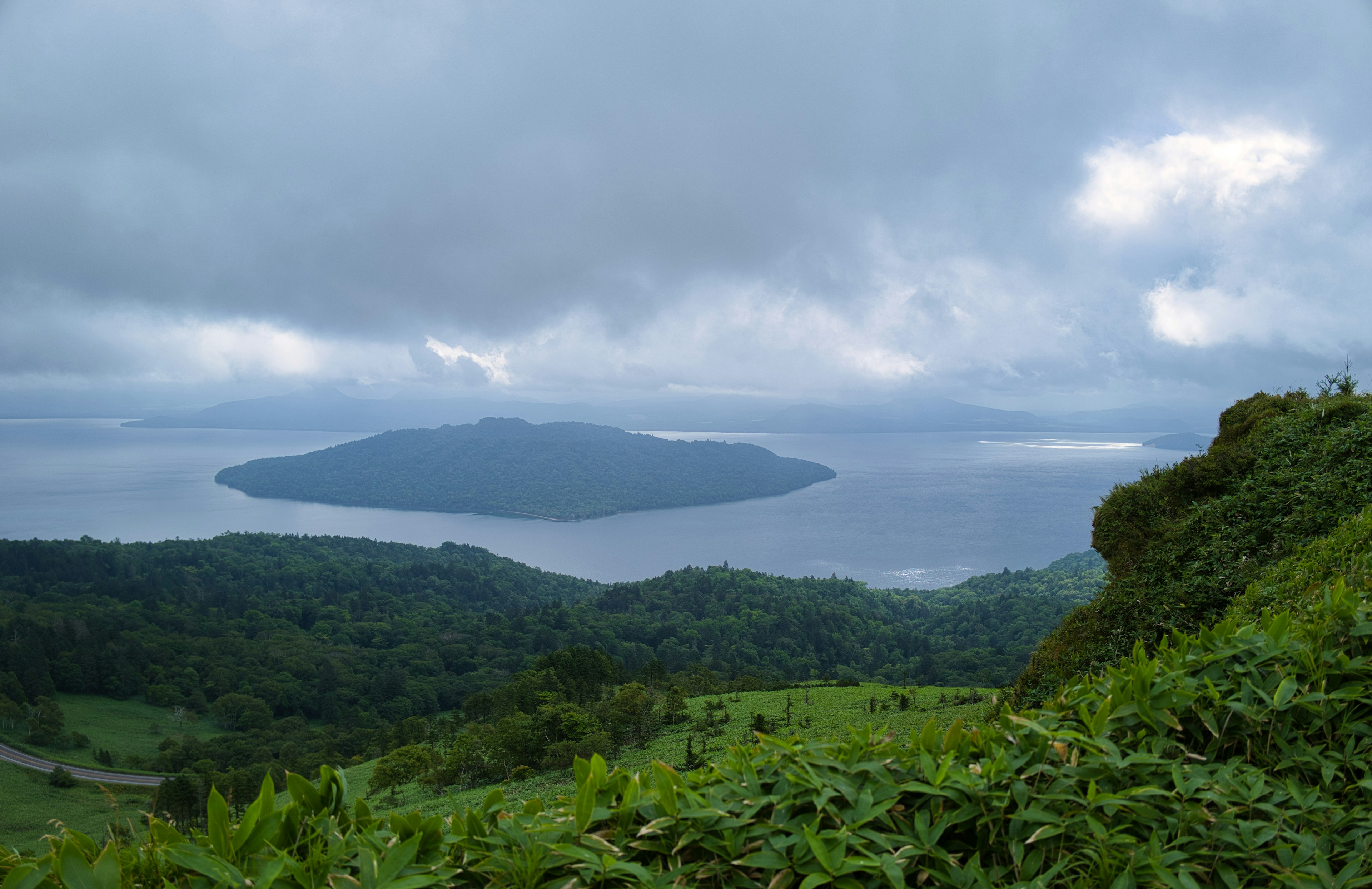 Pemandangan dari gunung menunjukkan pepohonan hijau dan pulau di bawah langit mendung