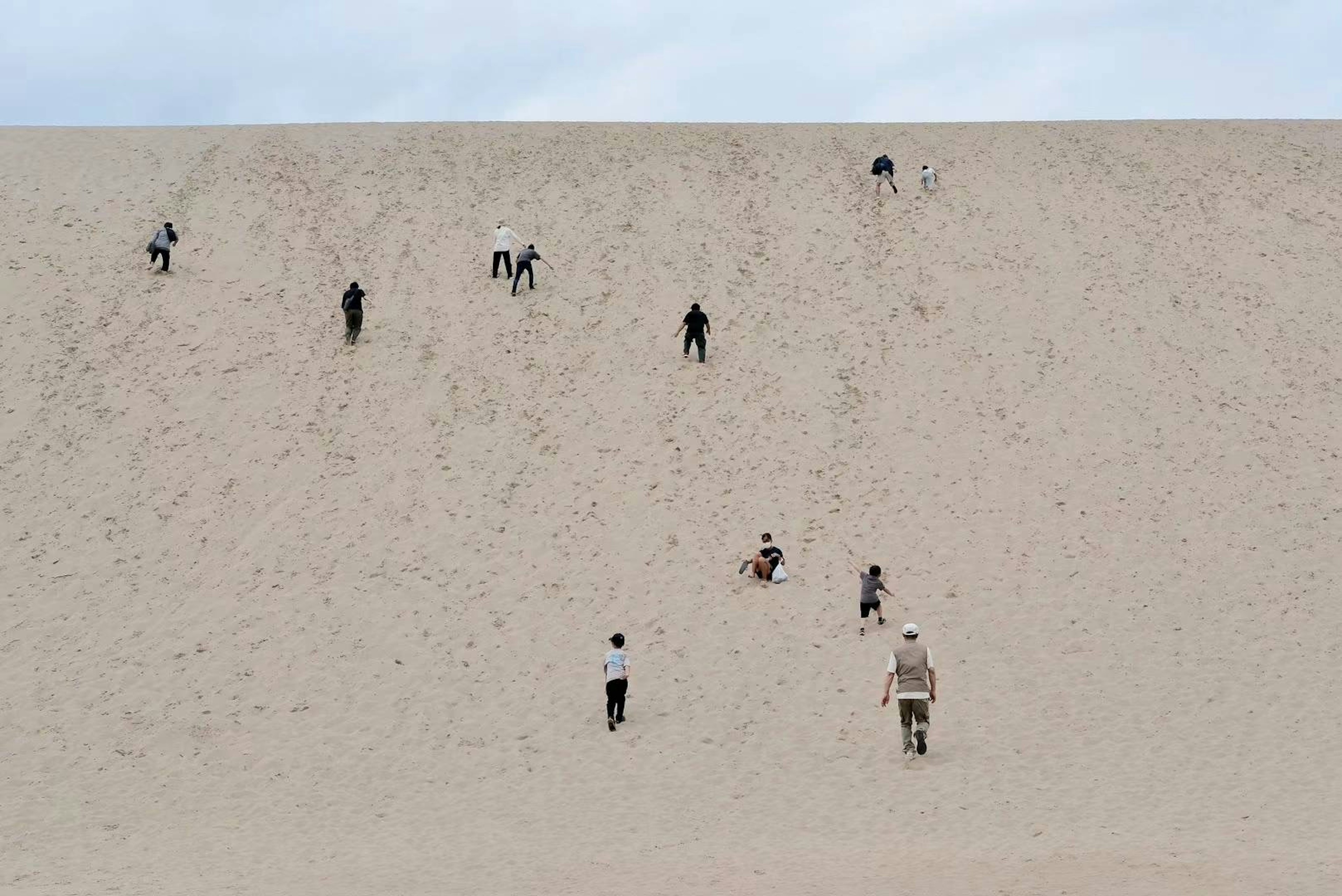 Des personnes grimpant sur une dune de sable sous un ciel bleu