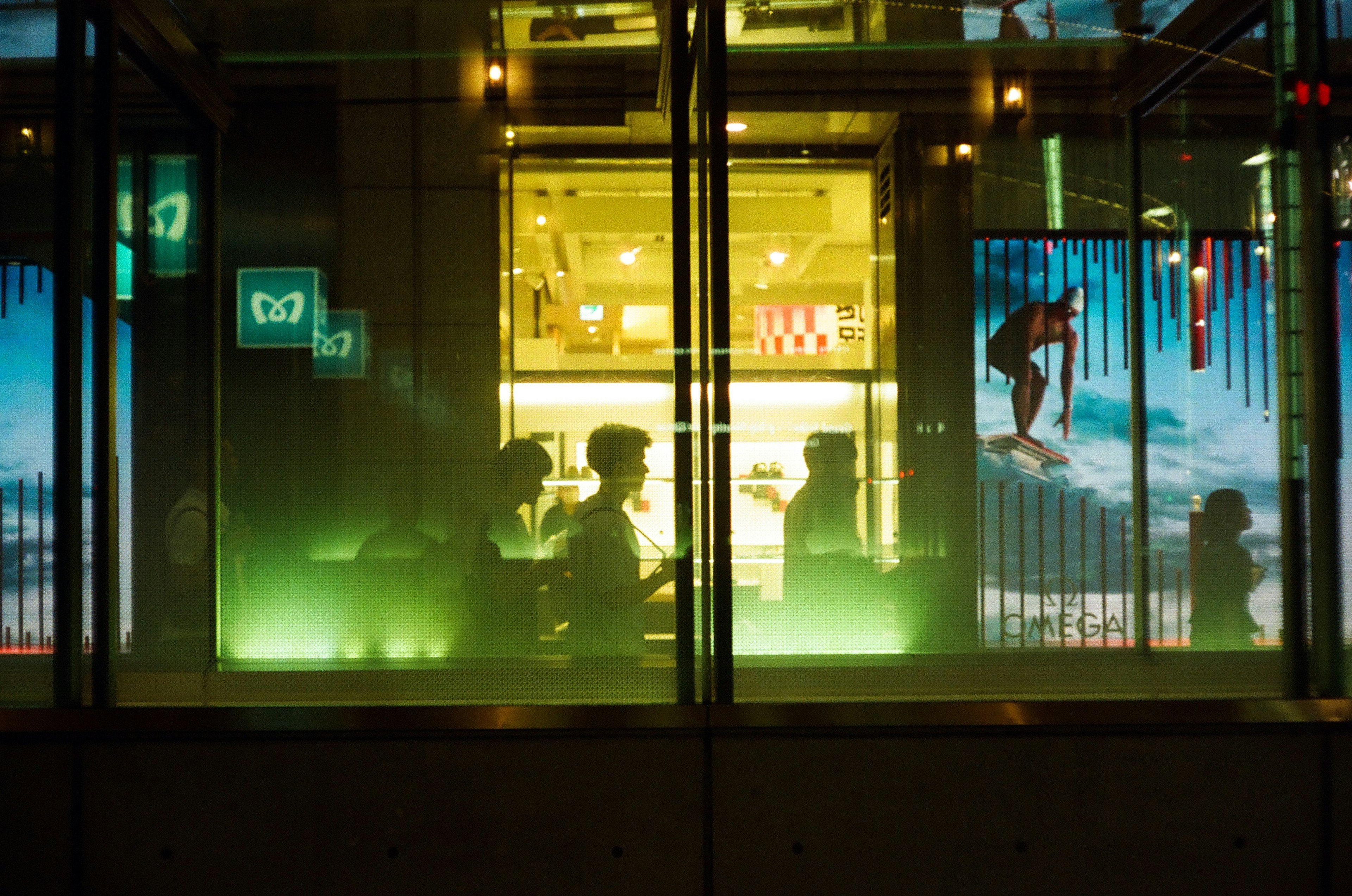 Night cityscape featuring silhouettes of people behind glass with colorful advertisements and green lighting