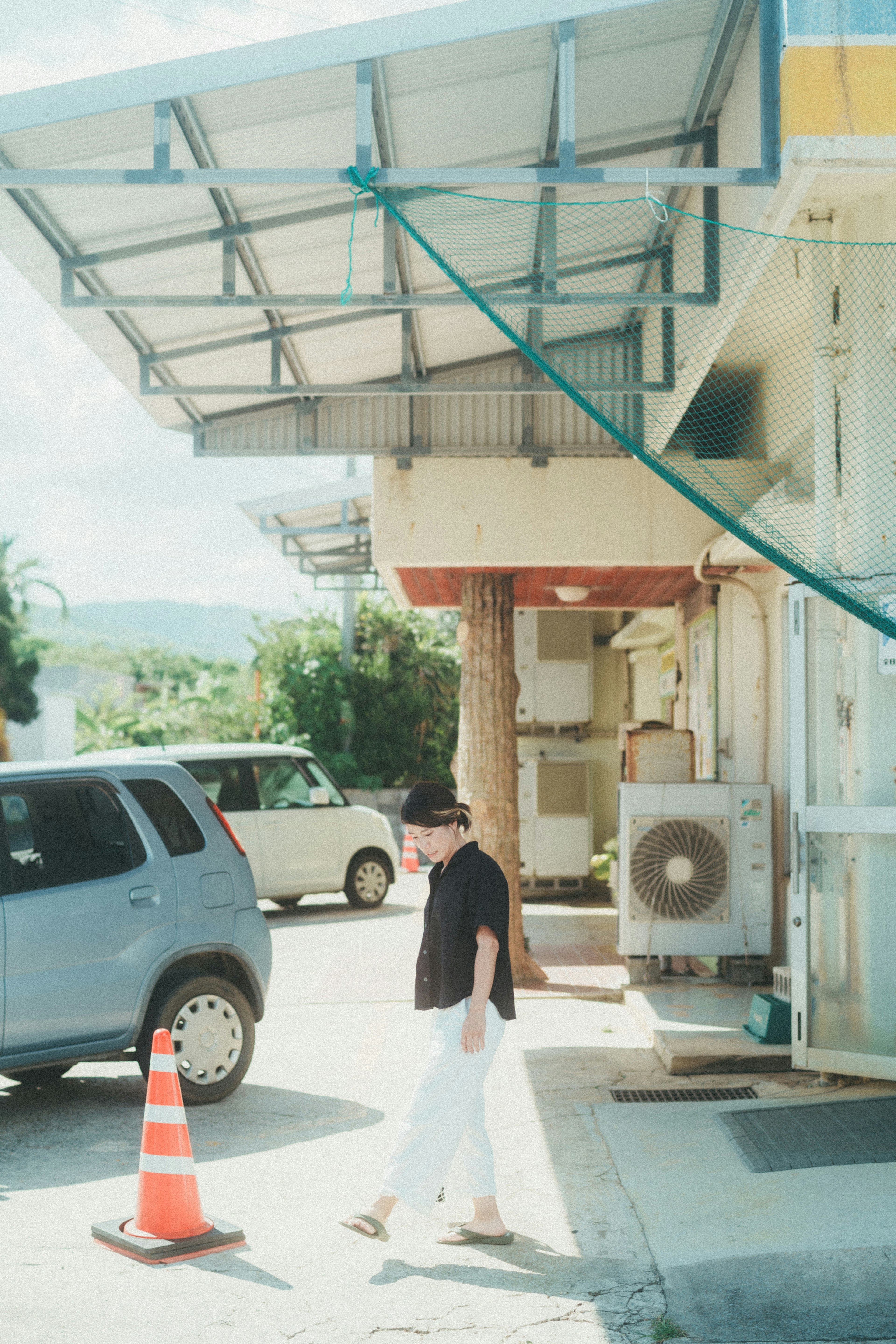 Person walking past a blue car and an orange cone