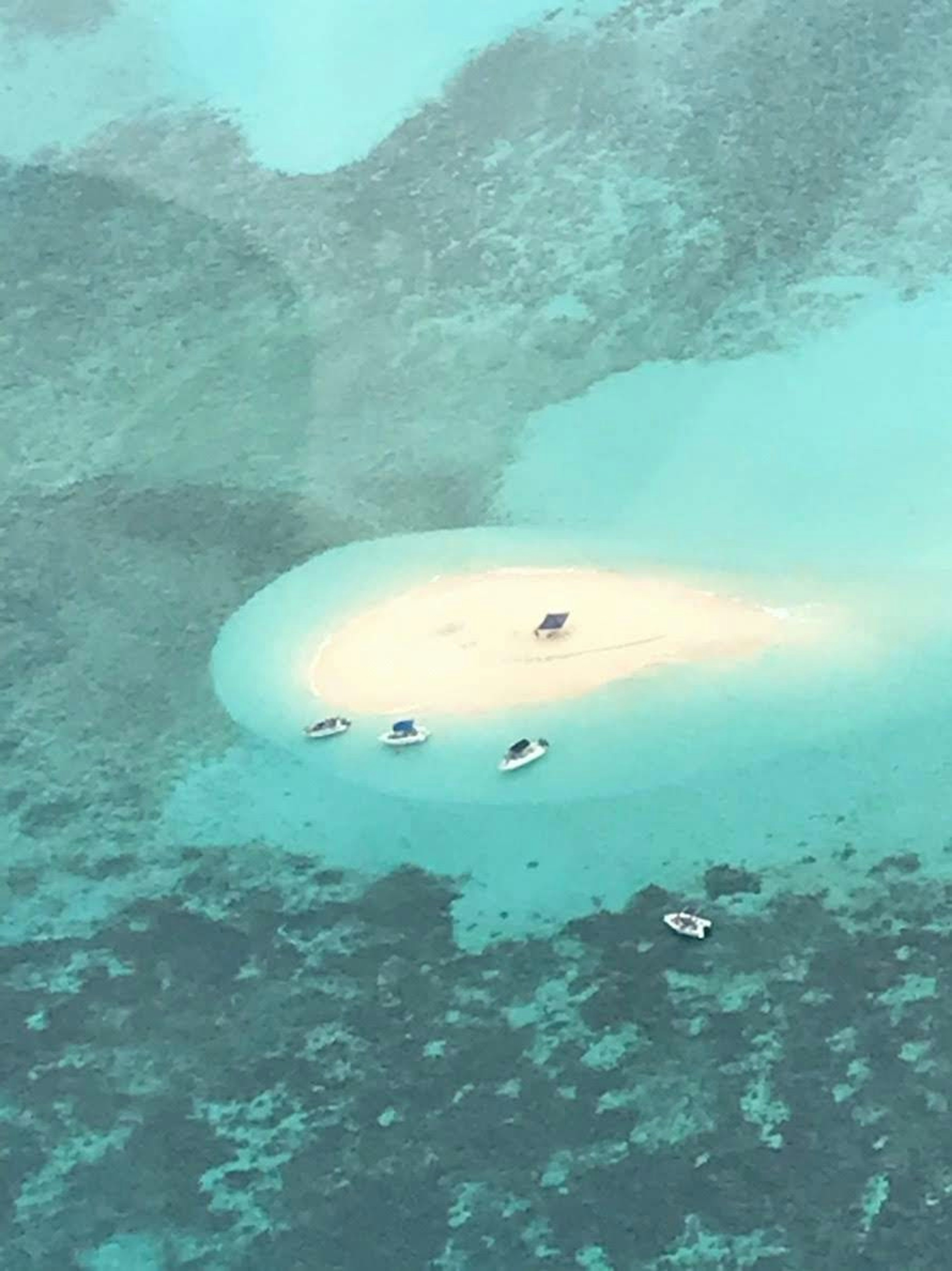 Vista aérea de un pequeño banco de arena rodeado de agua turquesa con barcos cercanos