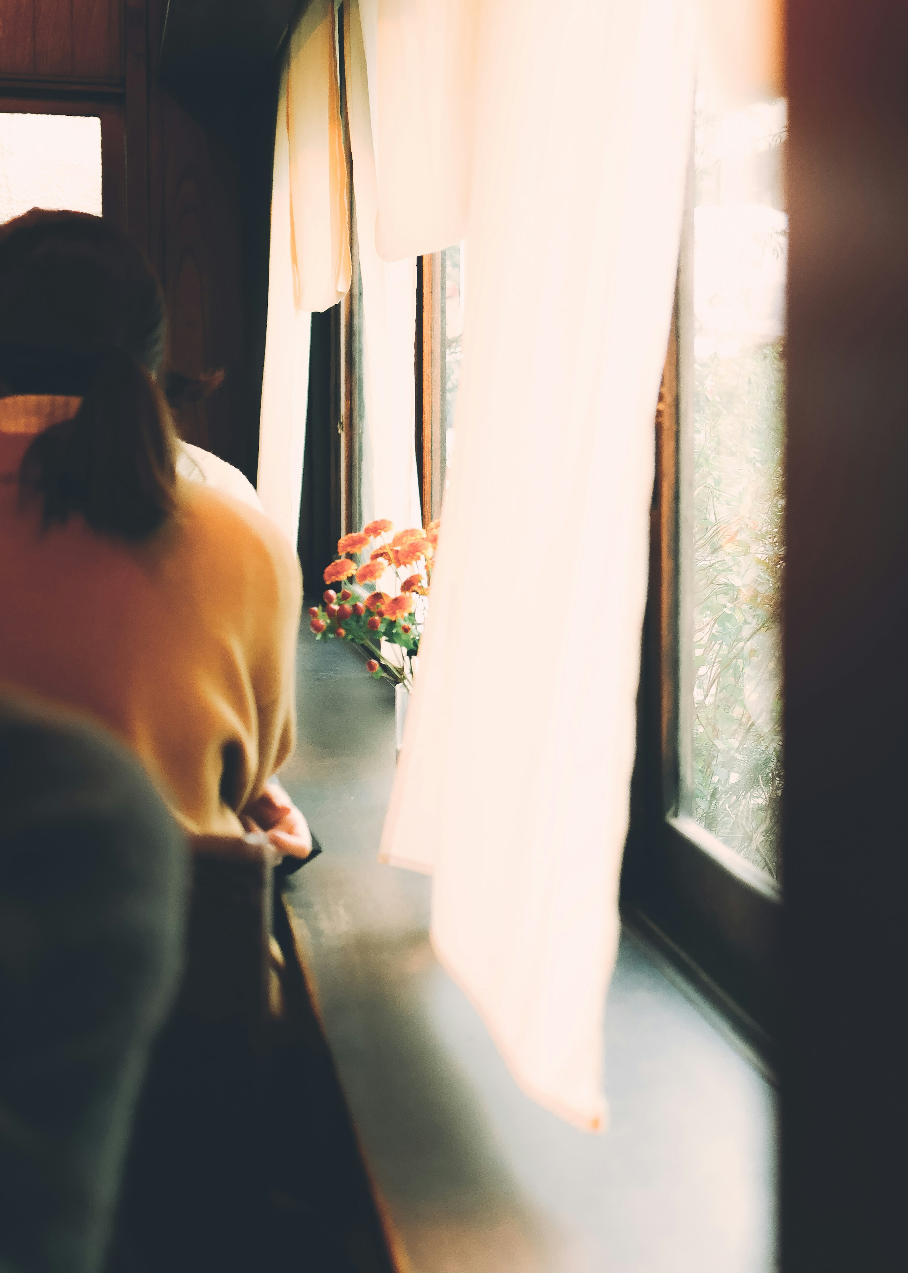 Person sitzt am Fenster mit sanftem Licht und Blumen