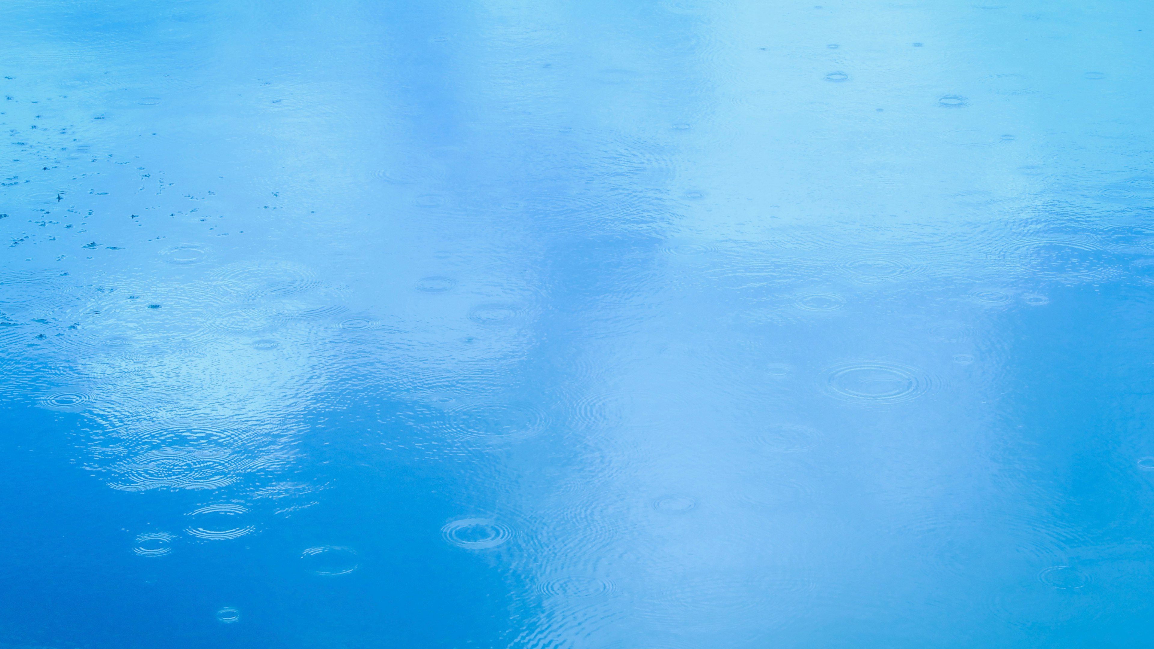 A blue water surface reflecting clouds with raindrops