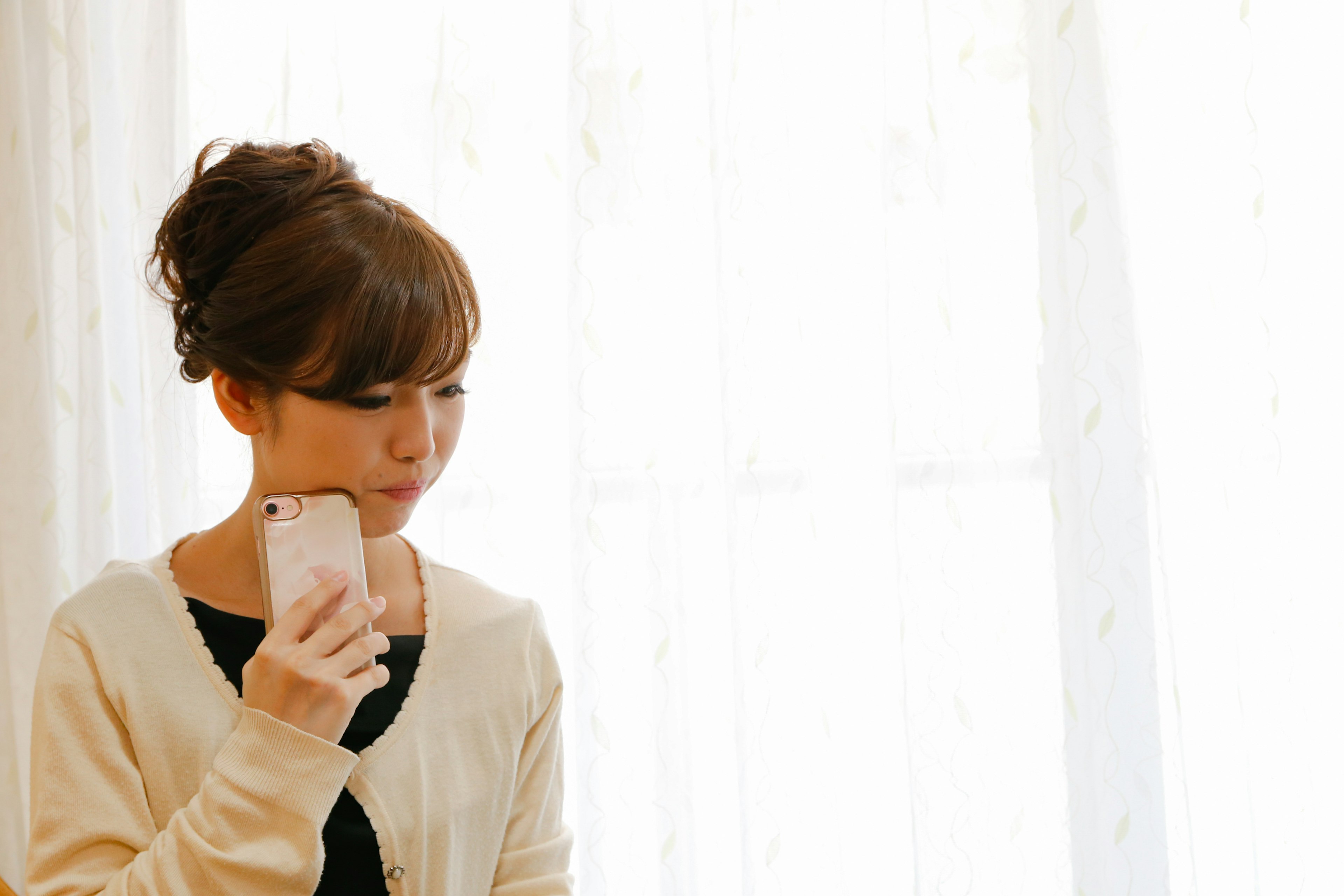 A woman standing by a window holding a smartphone