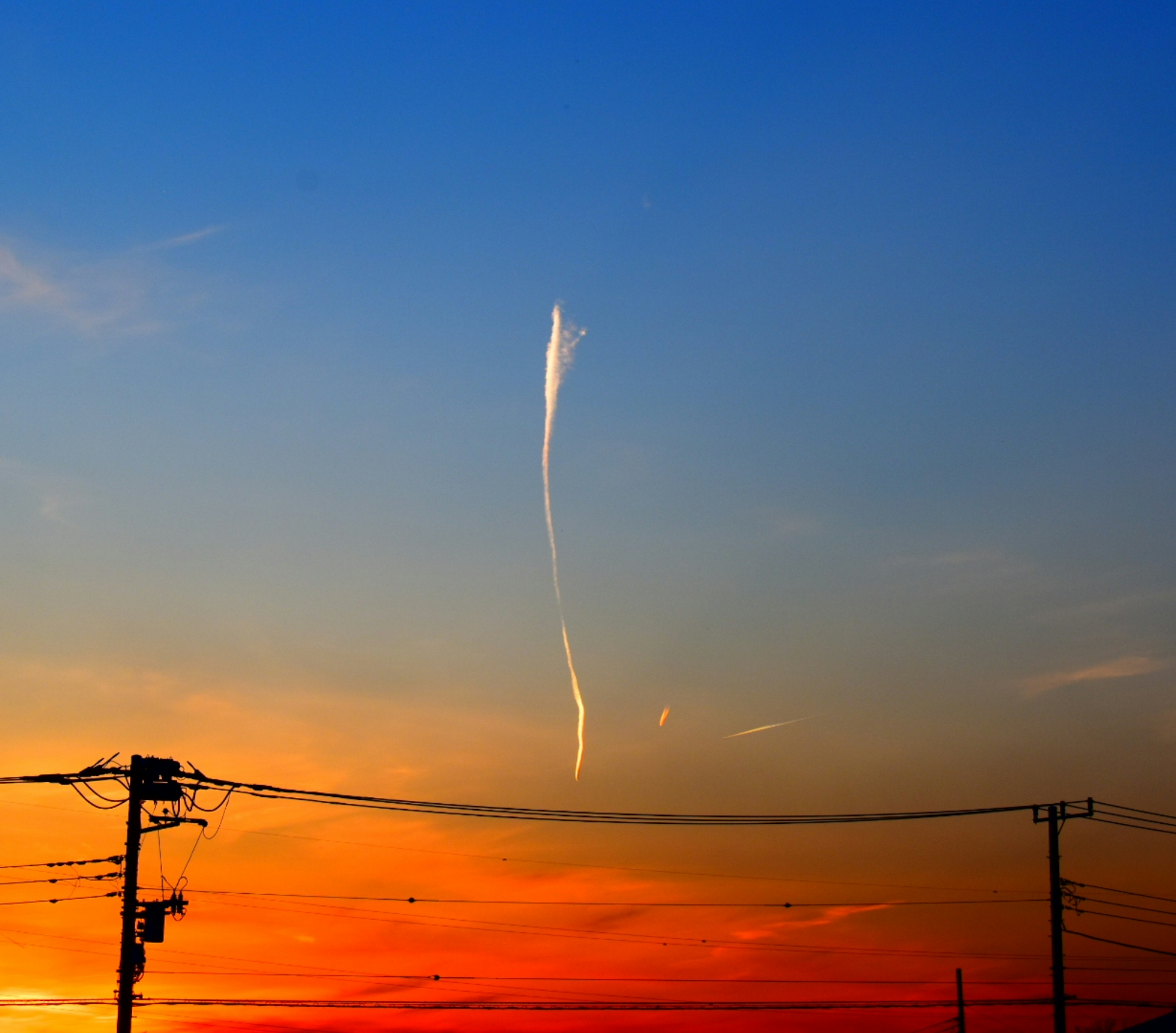 Sonnenuntergangshimmel mit einer schlanken Wolke und Stromleitungen