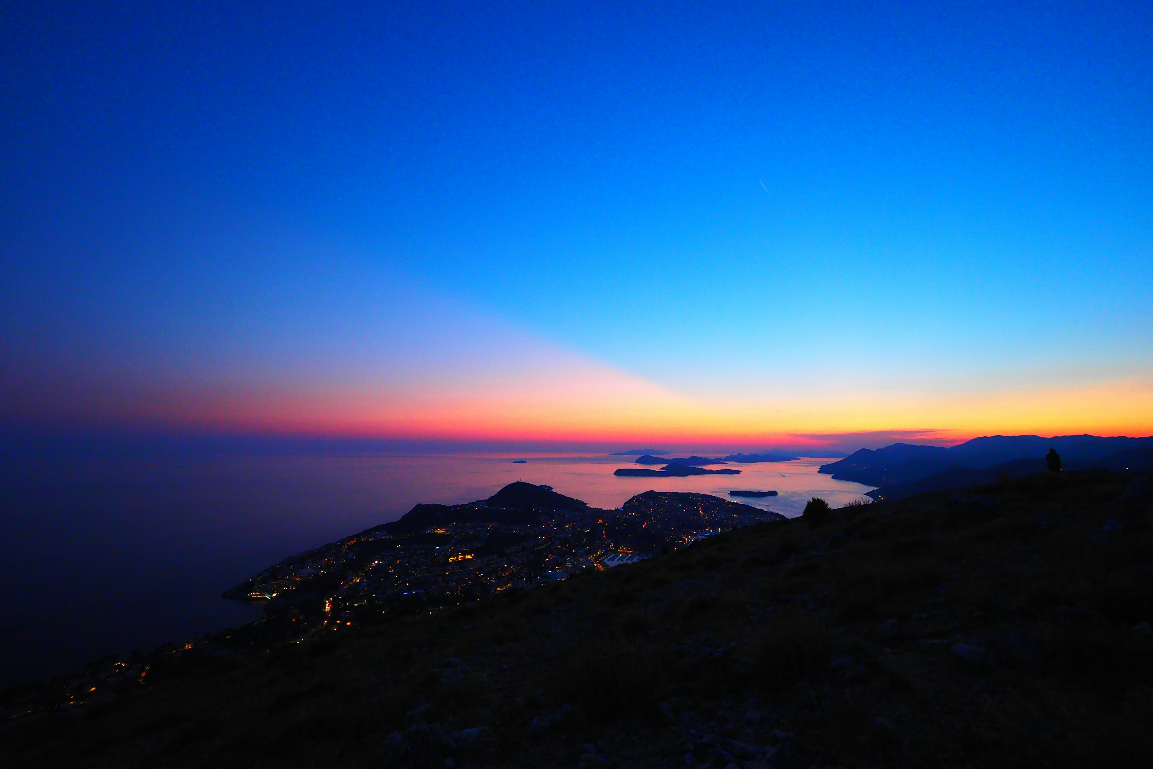 Atardecer sobre el mar con silueta de montaña luces de la ciudad brillando