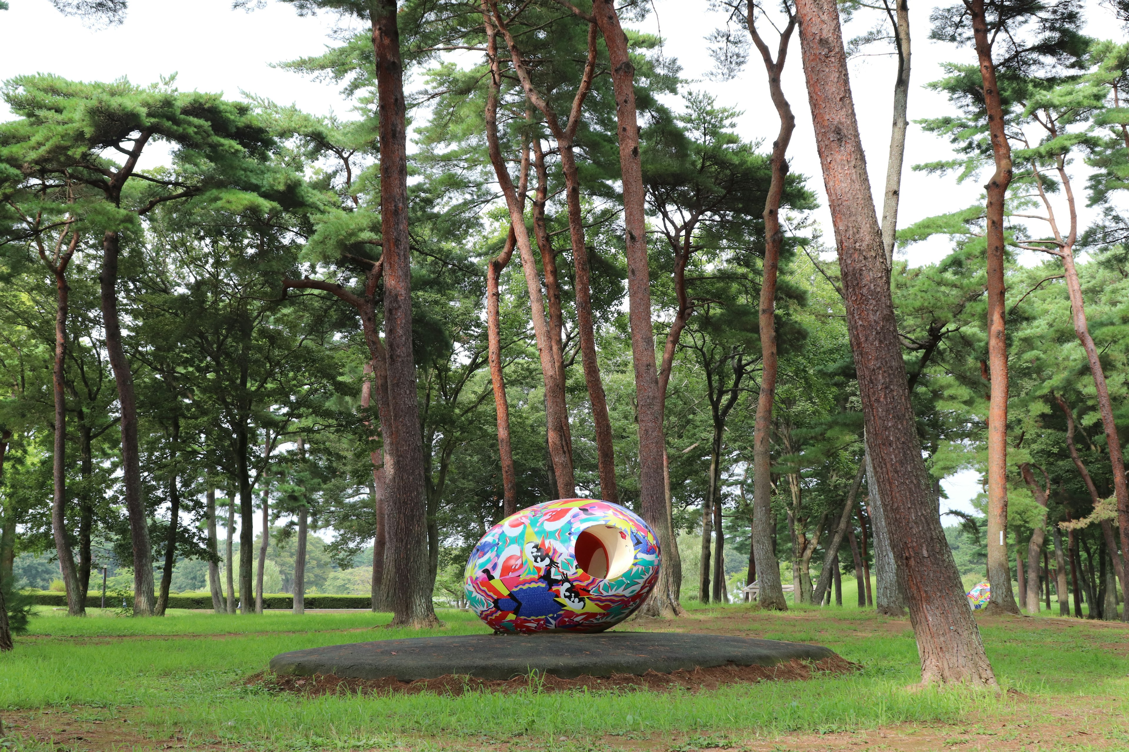 Una grande scultura a forma di uovo colorato è posizionata in una foresta verdeggiante