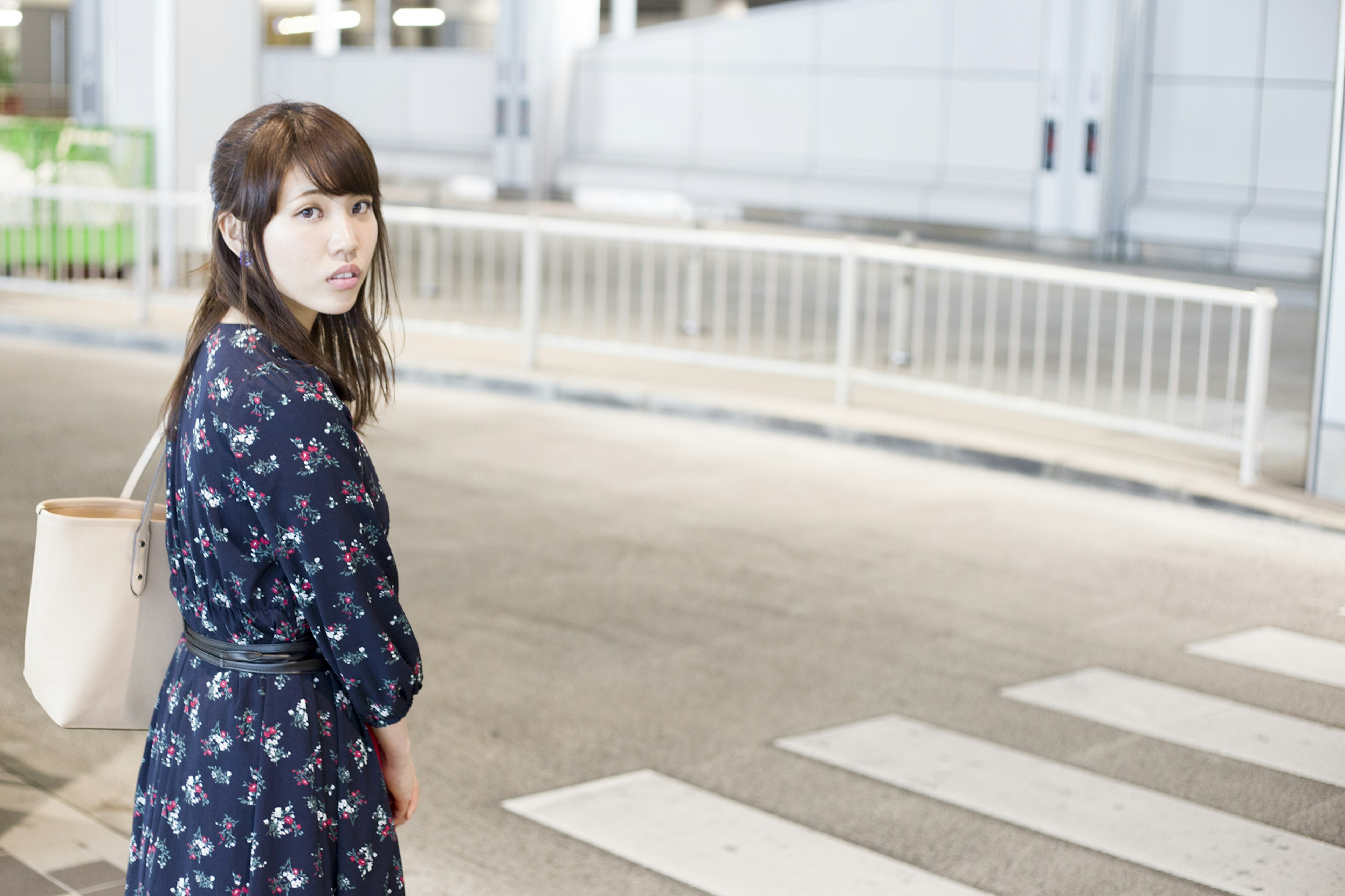 A woman standing at a crosswalk wearing a floral dress