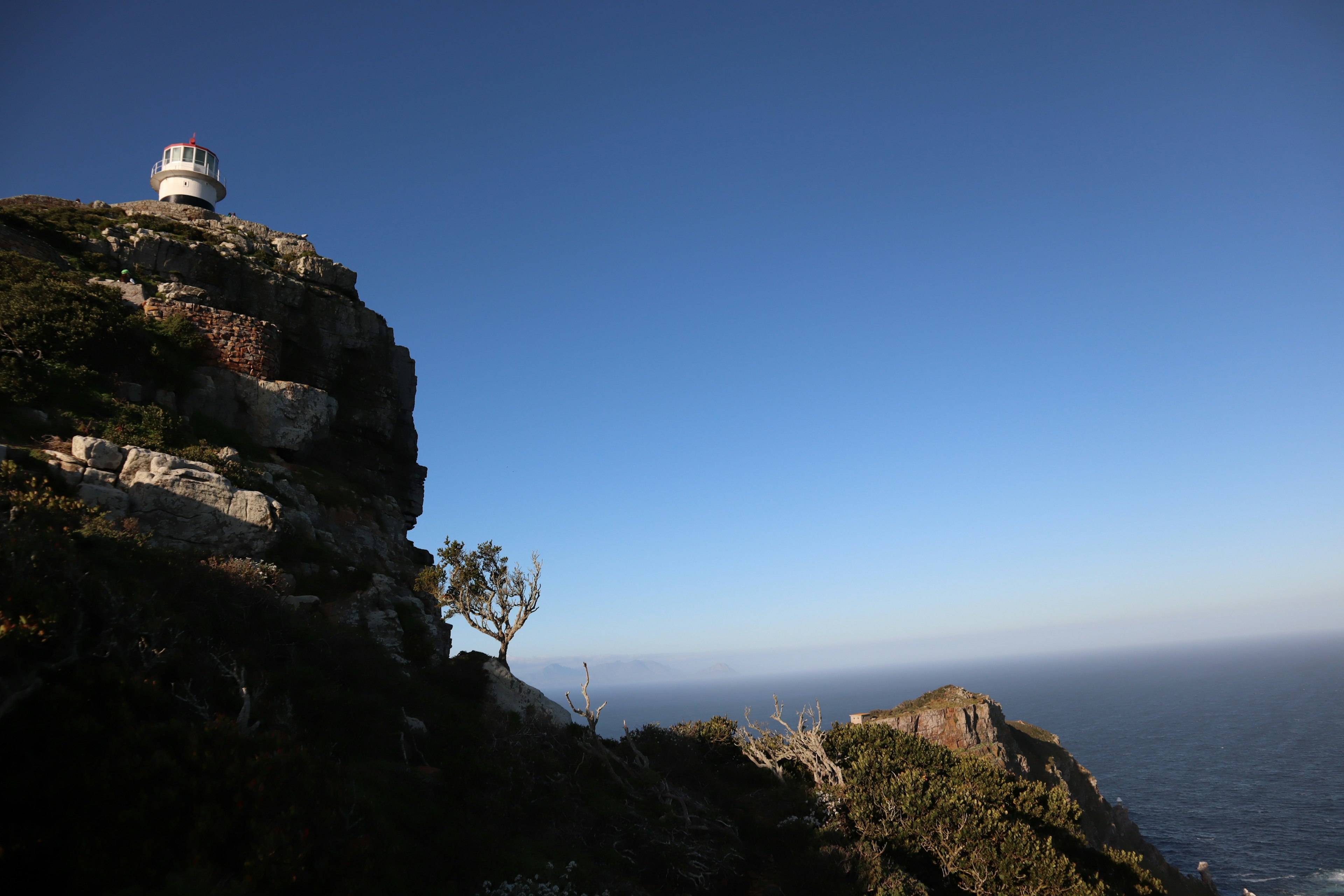 Scenic view of a coastal lighthouse on a rocky cliff with clear blue sky and ocean