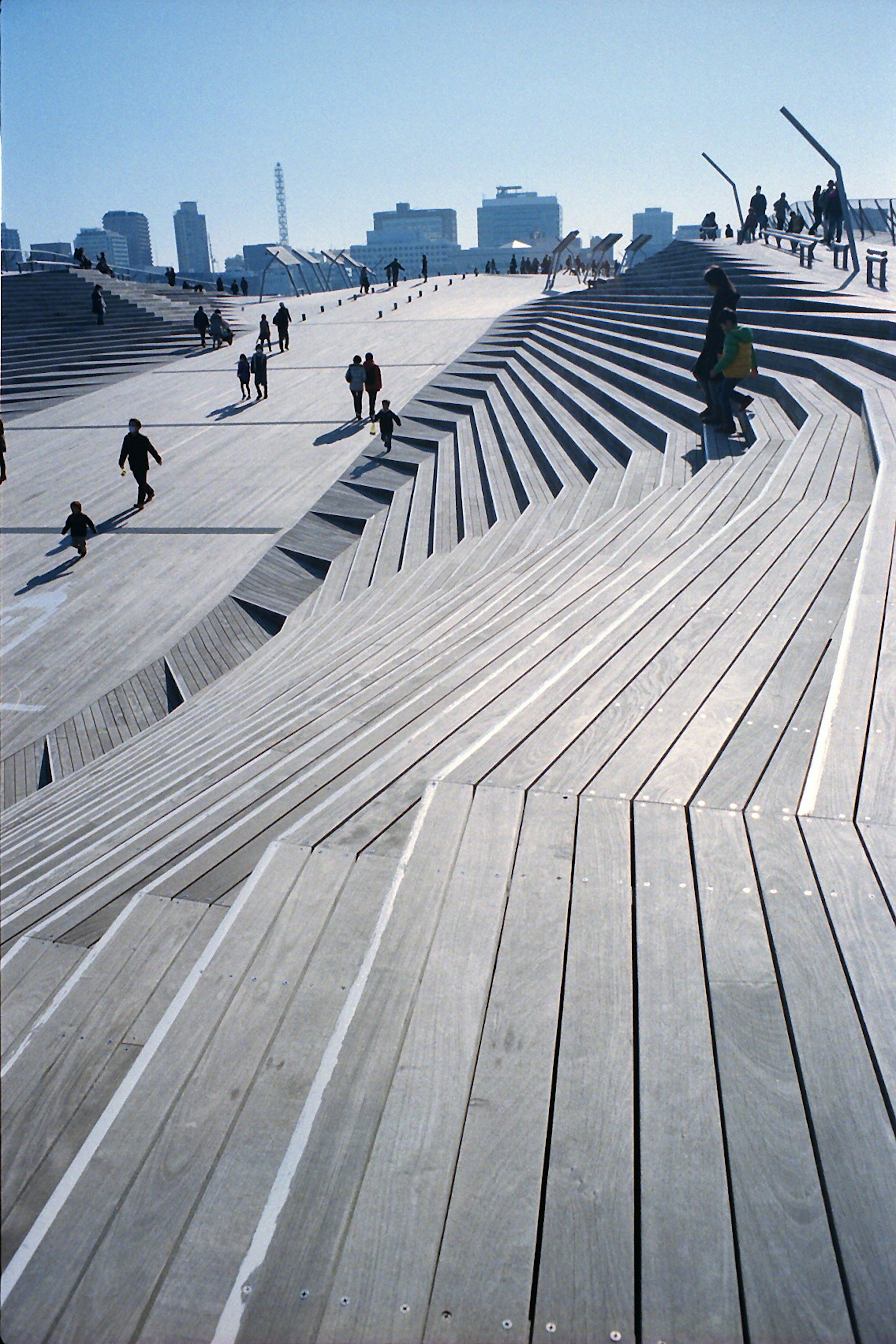 Personas caminando sobre escalones de madera ondulados con un cielo azul claro