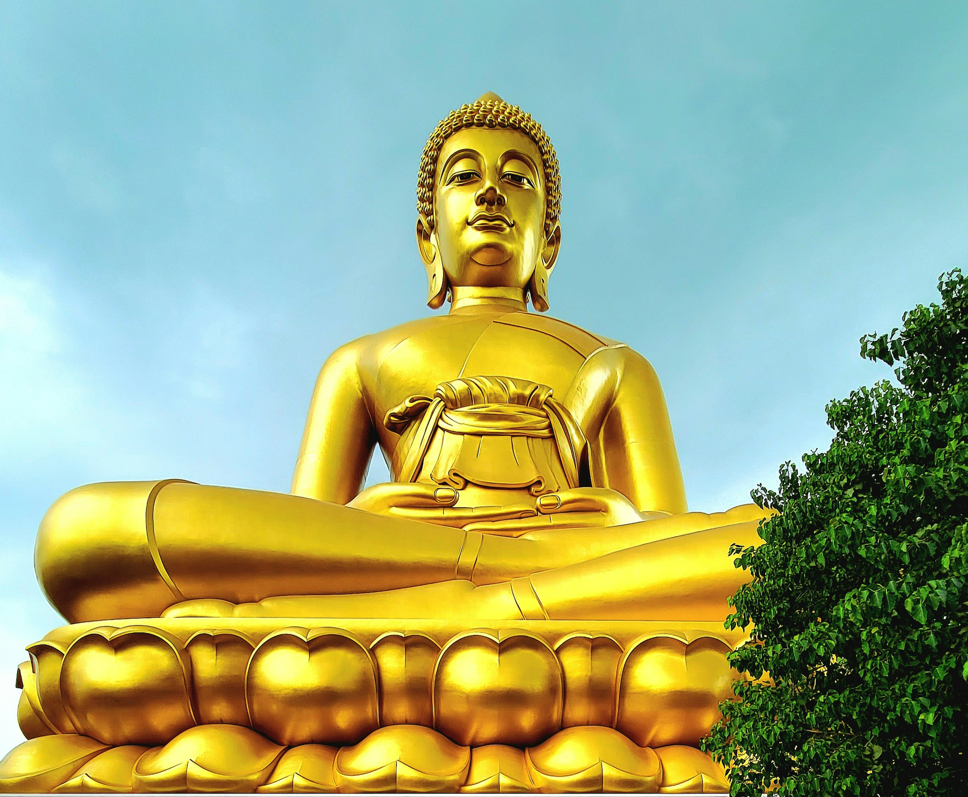 Statua di Buddha dorata seduta su uno sfondo di cielo blu e alberi verdi