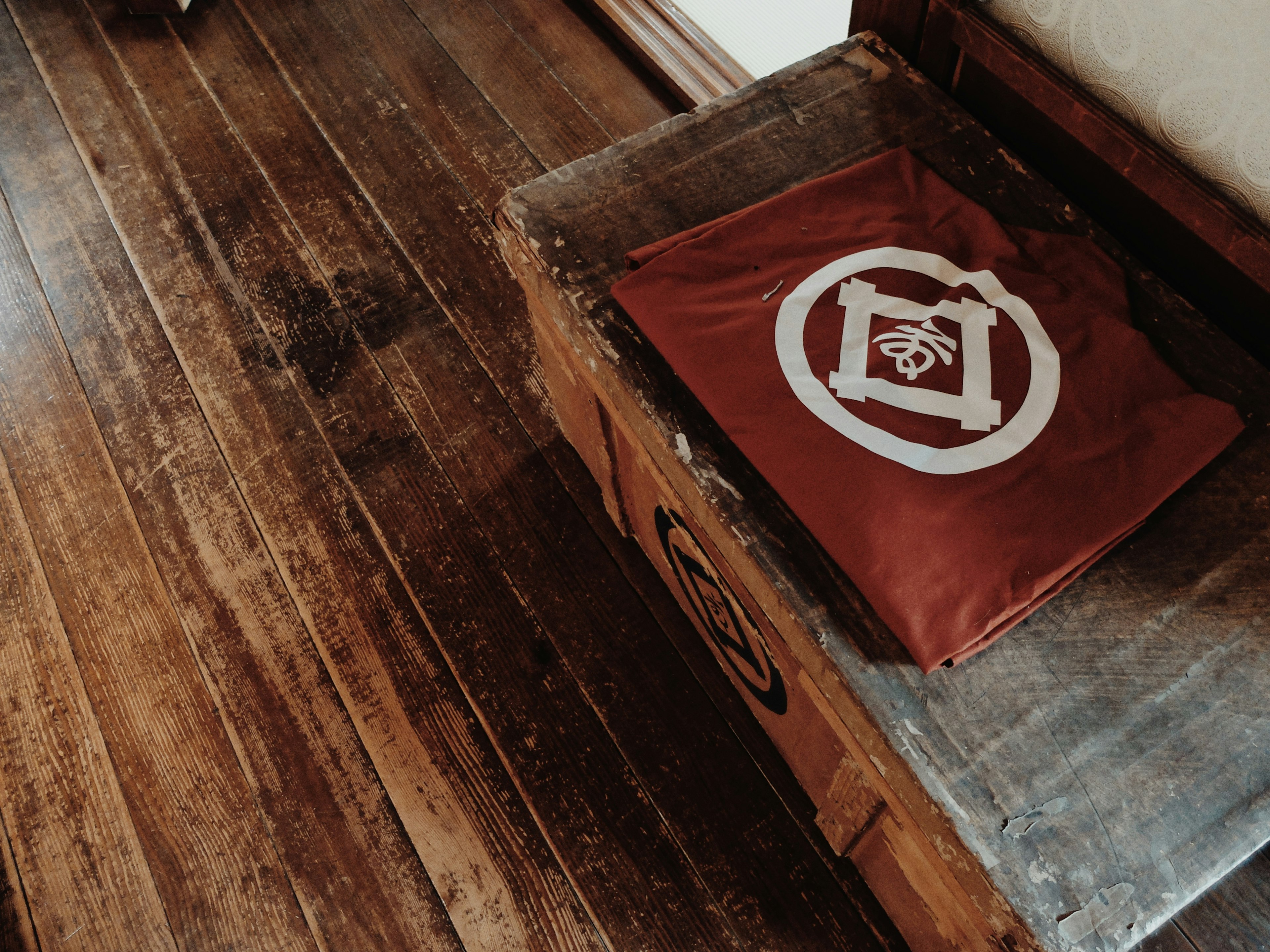 A wooden floor with a red fabric displaying a white logo on a rustic box