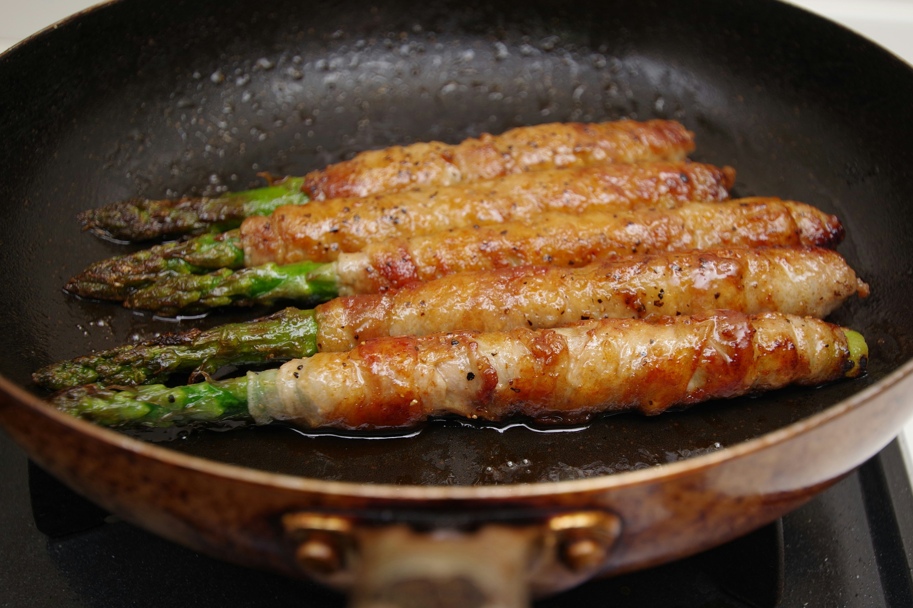 Bacon-wrapped asparagus cooking in a skillet