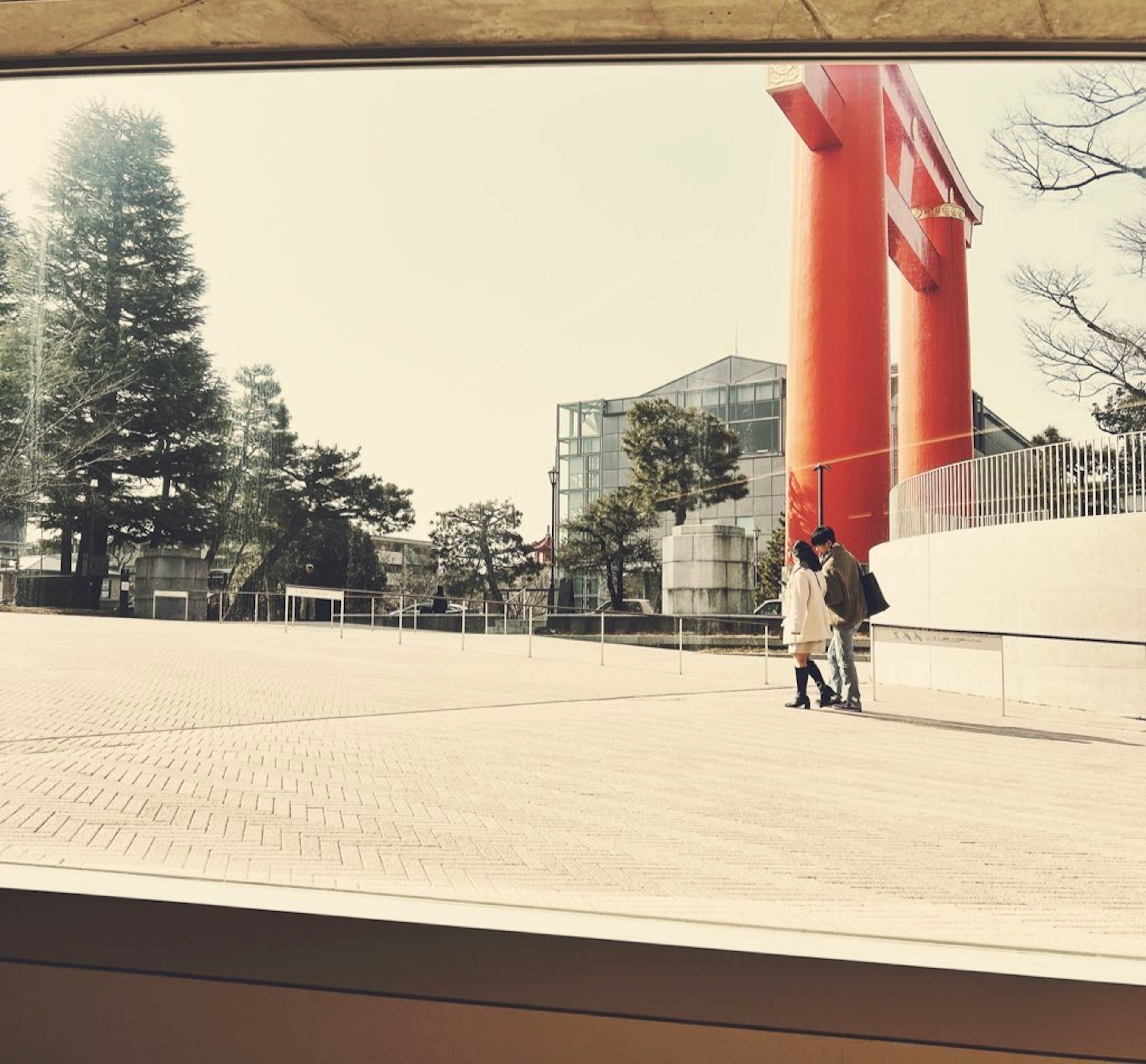 Two people walking in a plaza with a red torii gate and modern architecture