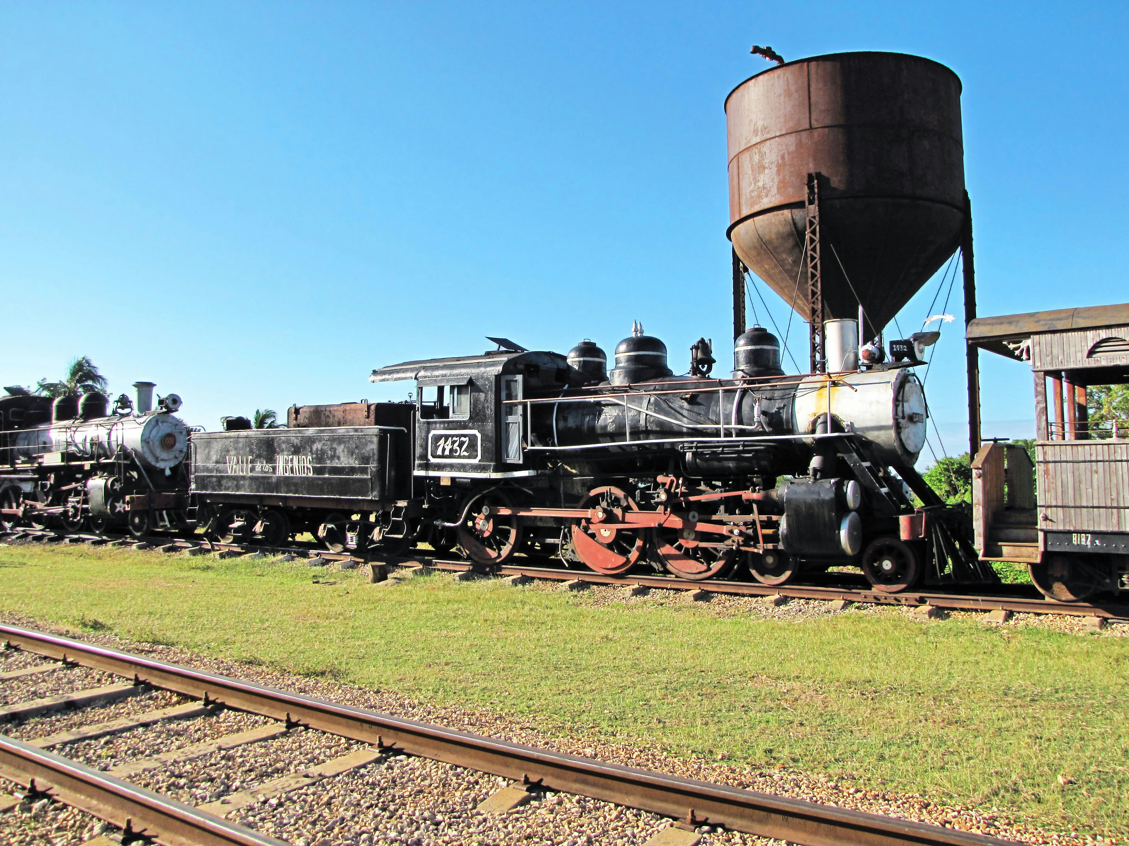 Locomotoras de vapor históricas alineadas cerca de un tanque de agua bajo un cielo azul claro