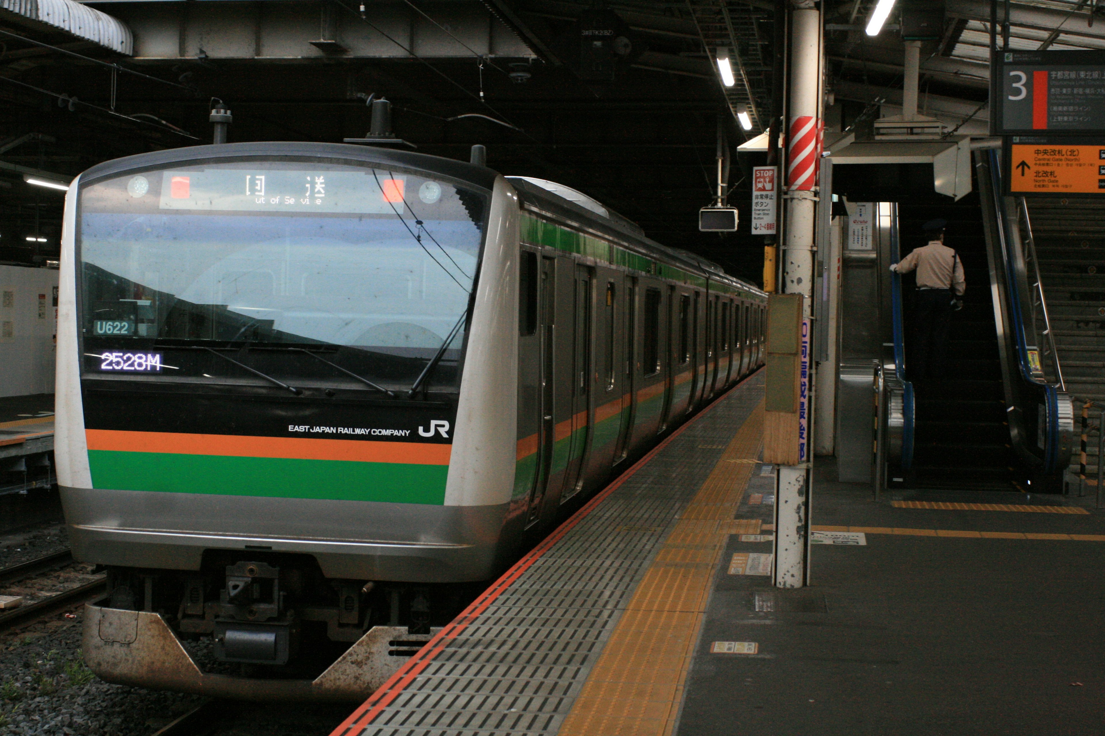 A Japanese train with green and orange stripes is stopped at a station