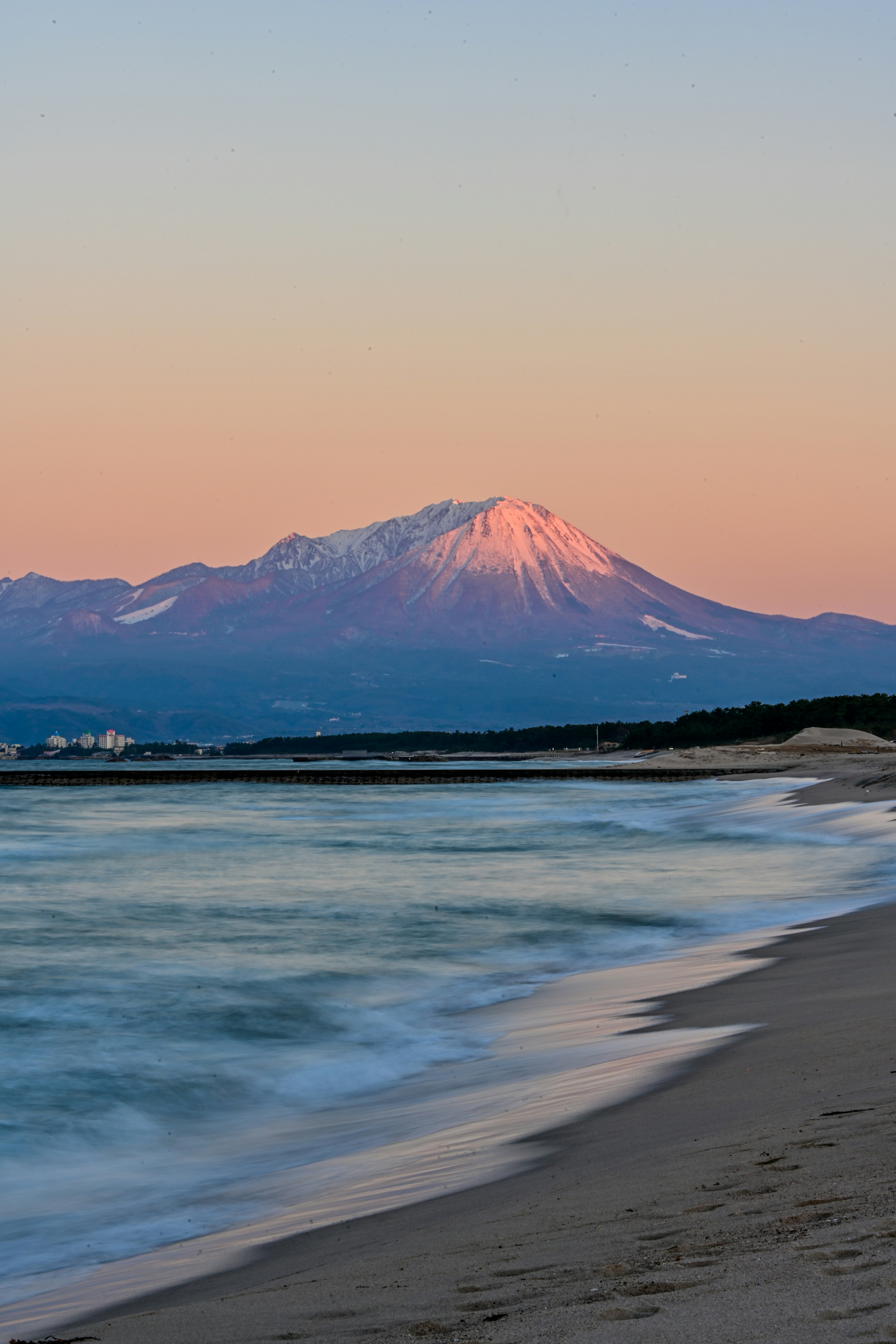 夕暮れの海岸線にそびえる雪をかぶった山