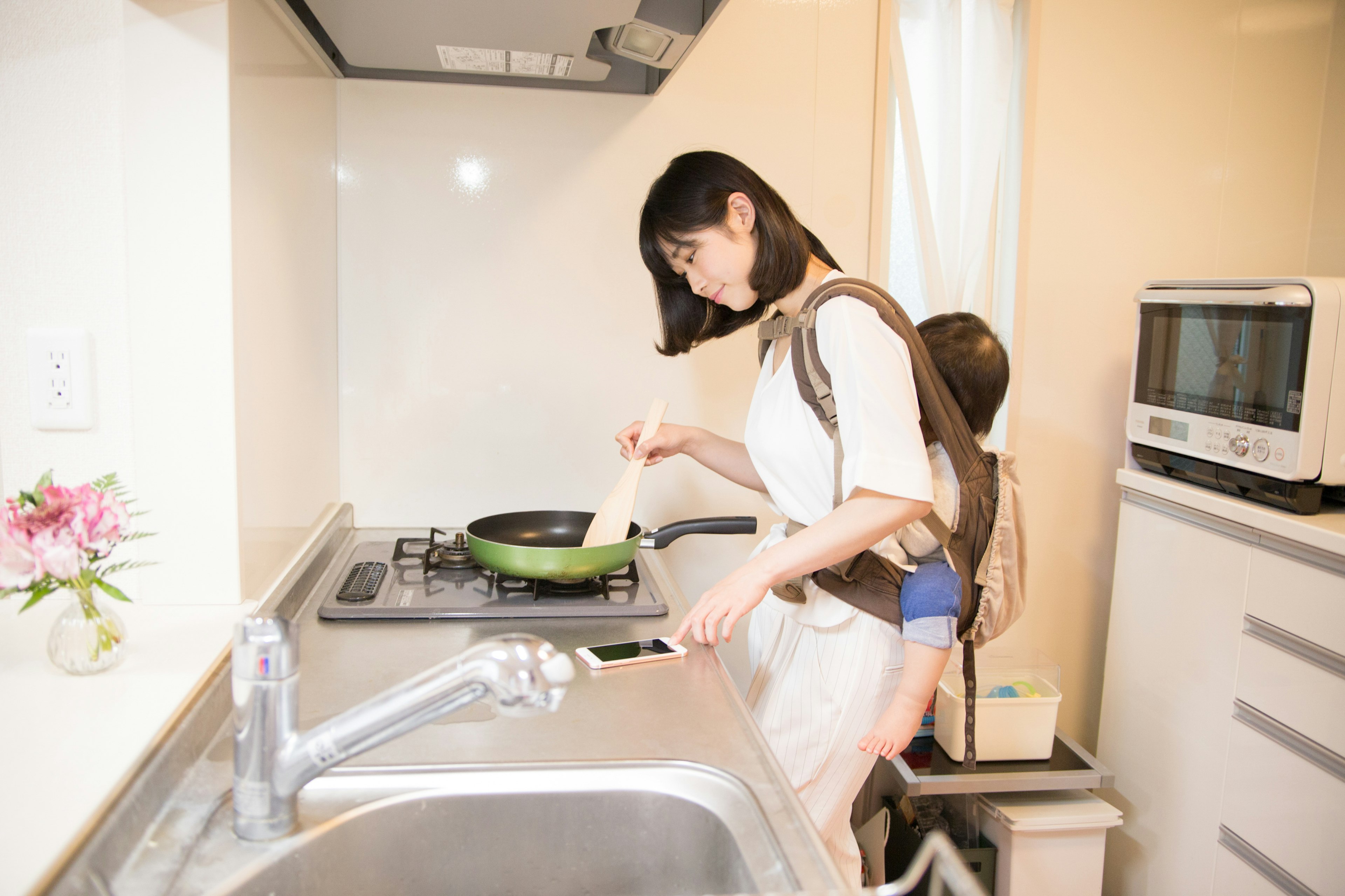 Una madre cocinando en la cocina mientras lleva a su hijo a la espalda