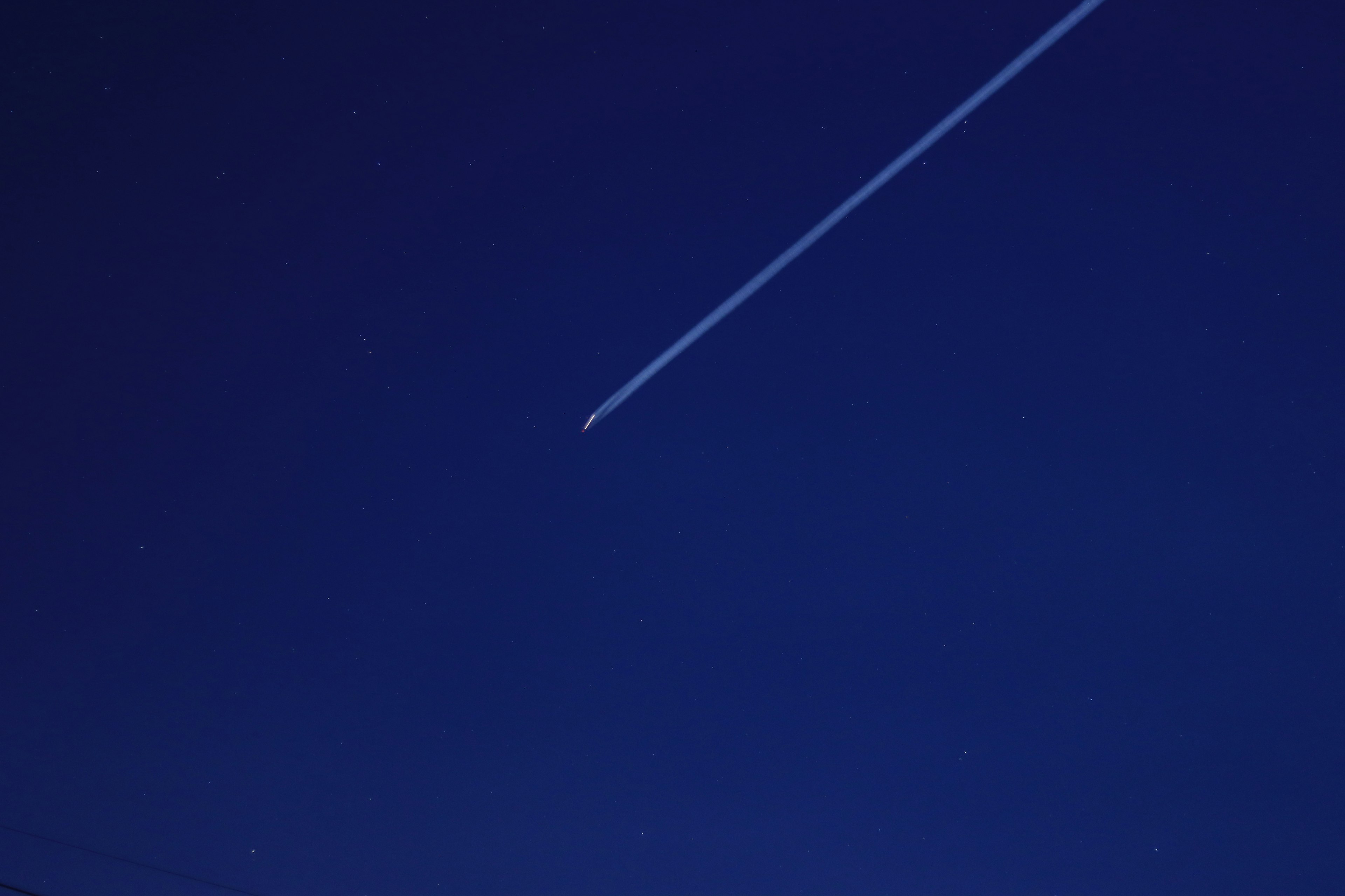 青い夜空に飛行機の飛行機雲が見える