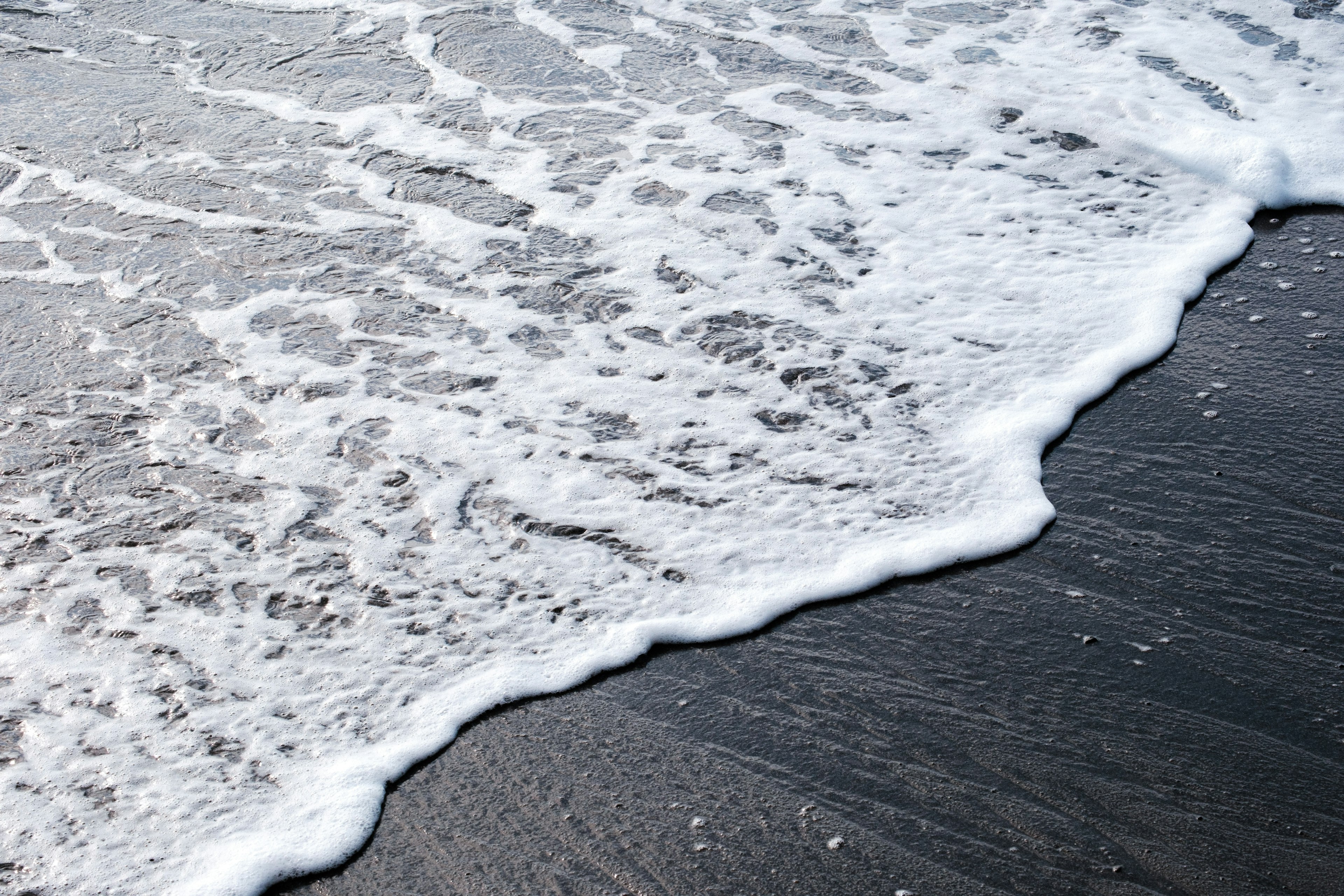 Weiße Schaumwellen an einem schwarzen Sandstrand