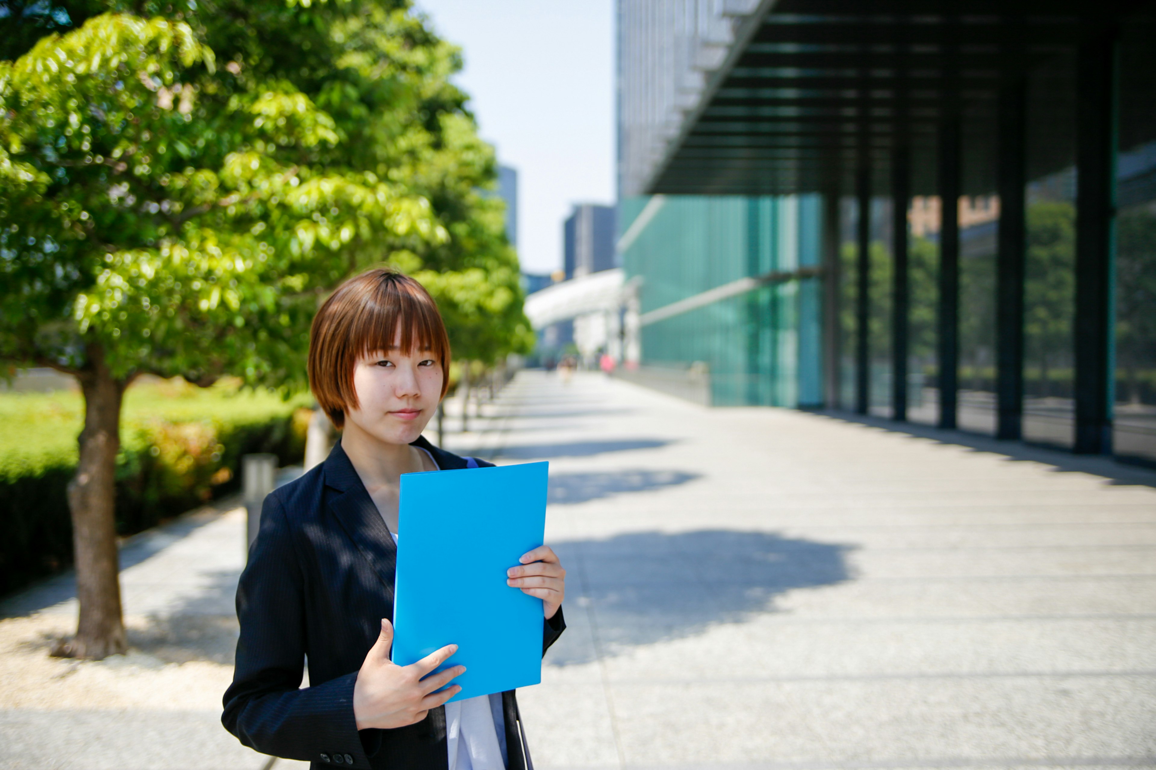 手持蓝色文件夹的女性商务人士站在现代建筑前