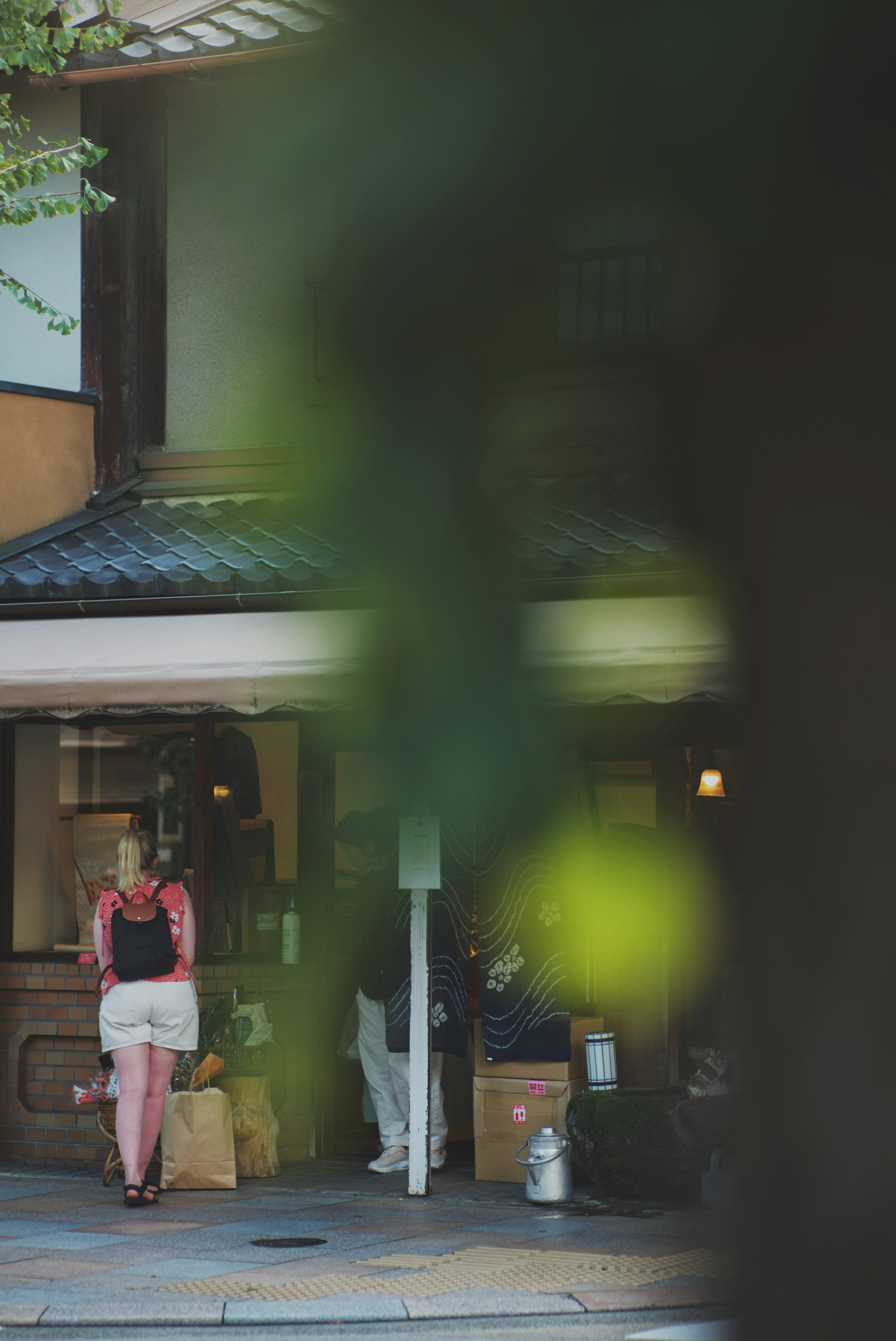 一位女性站在商店前面，前景有綠色植物