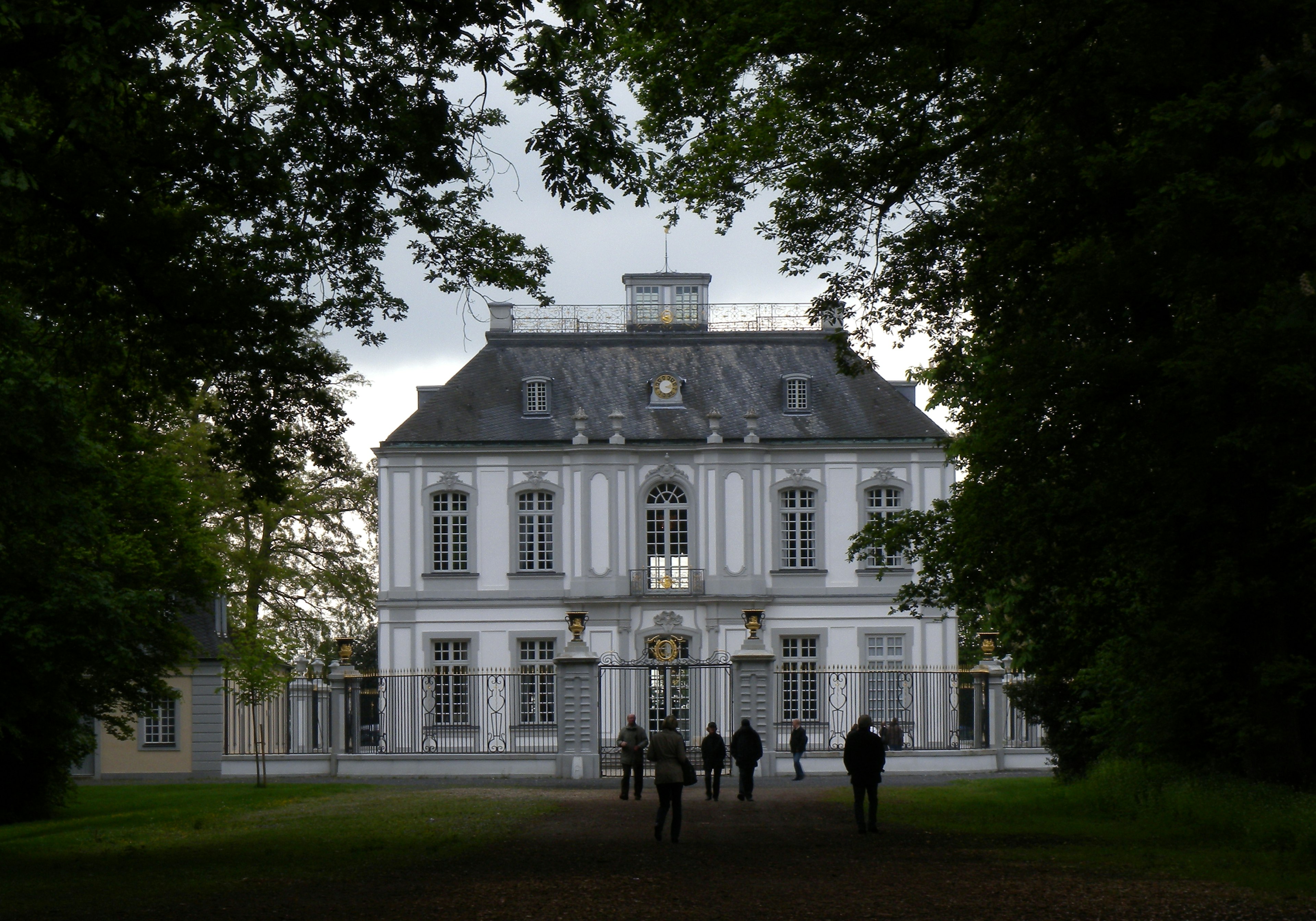 Un bâtiment blanc entouré de verdure avec des personnes s'approchant