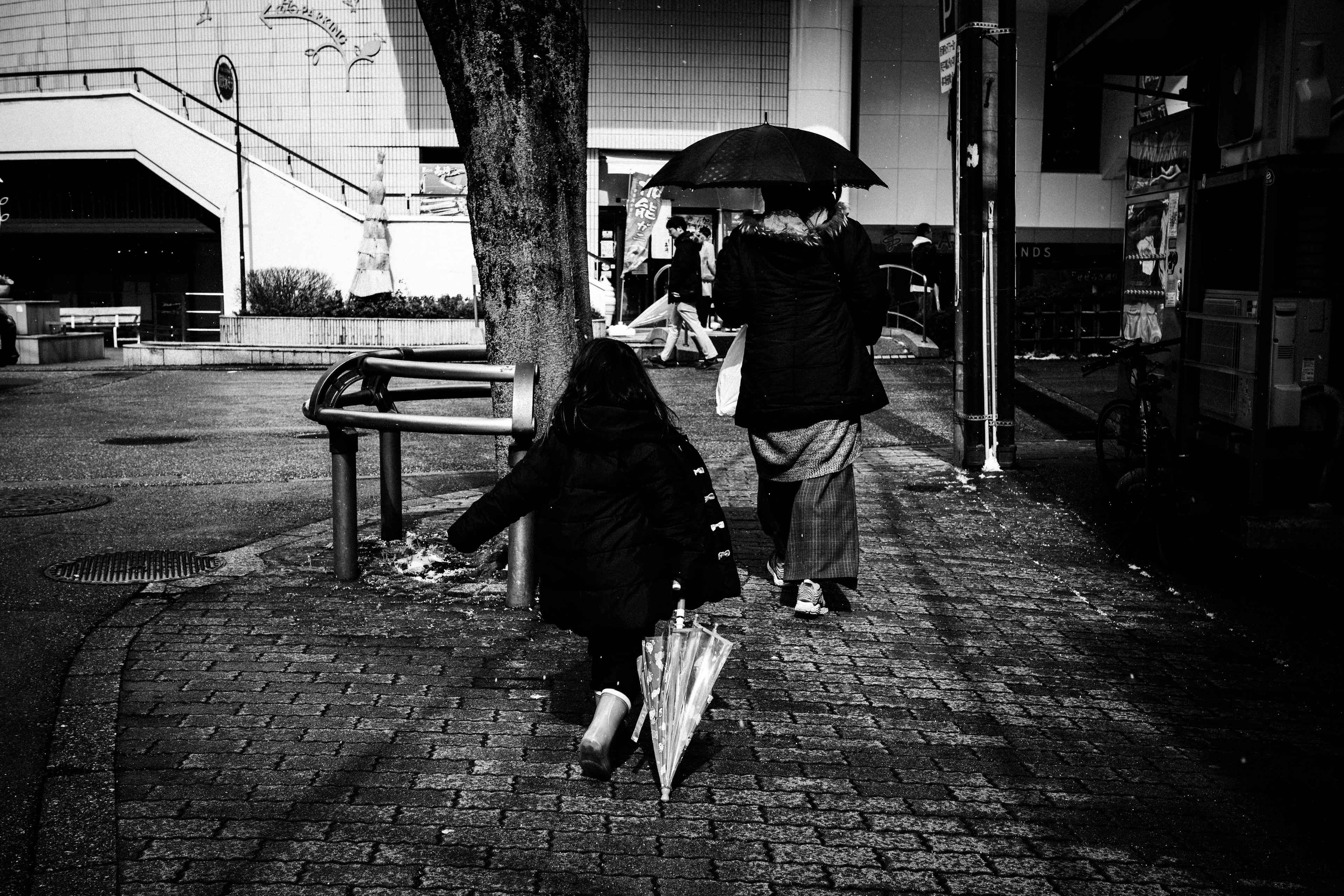 Ein Erwachsener mit einem Regenschirm und ein kleines Kind, das in einer schwarz-weißen städtischen Umgebung geht