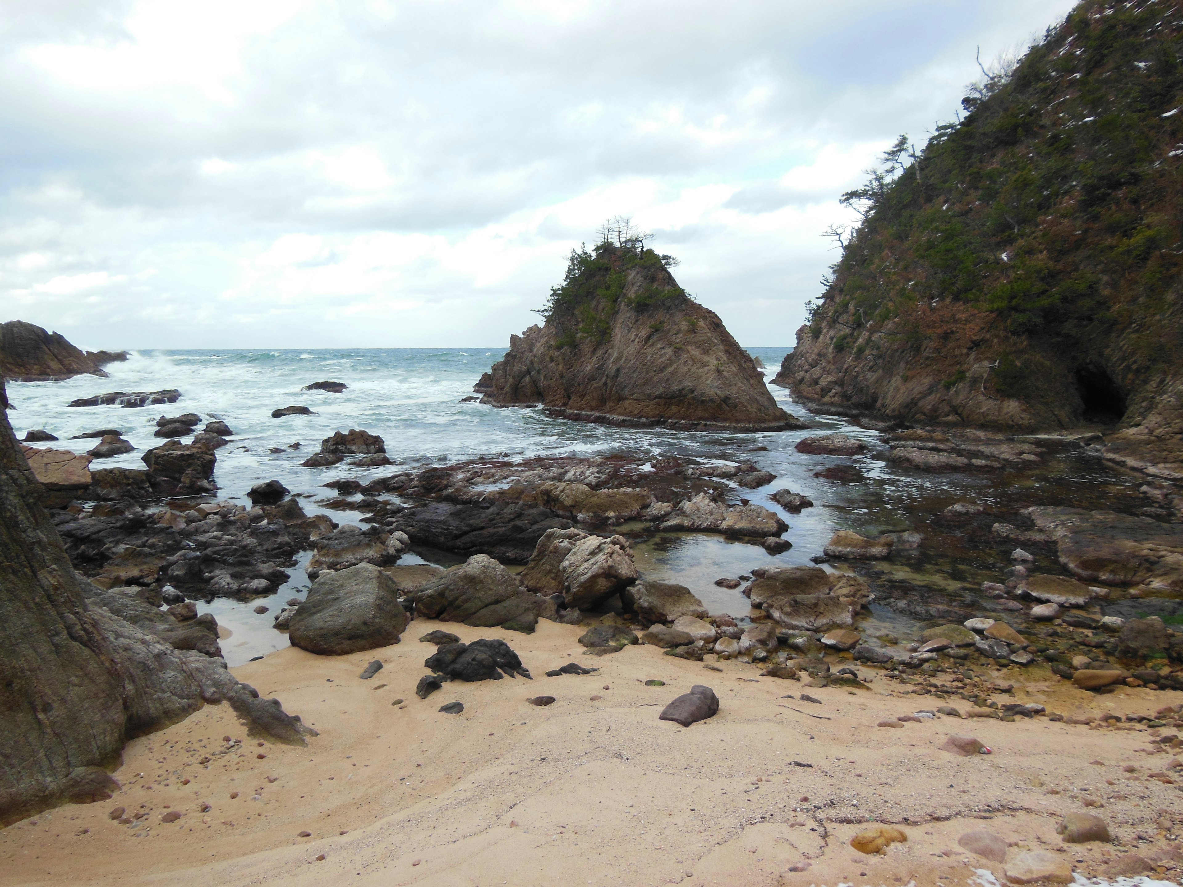 Vista costera con rocas y playa de arena cielo nublado y olas tranquilas