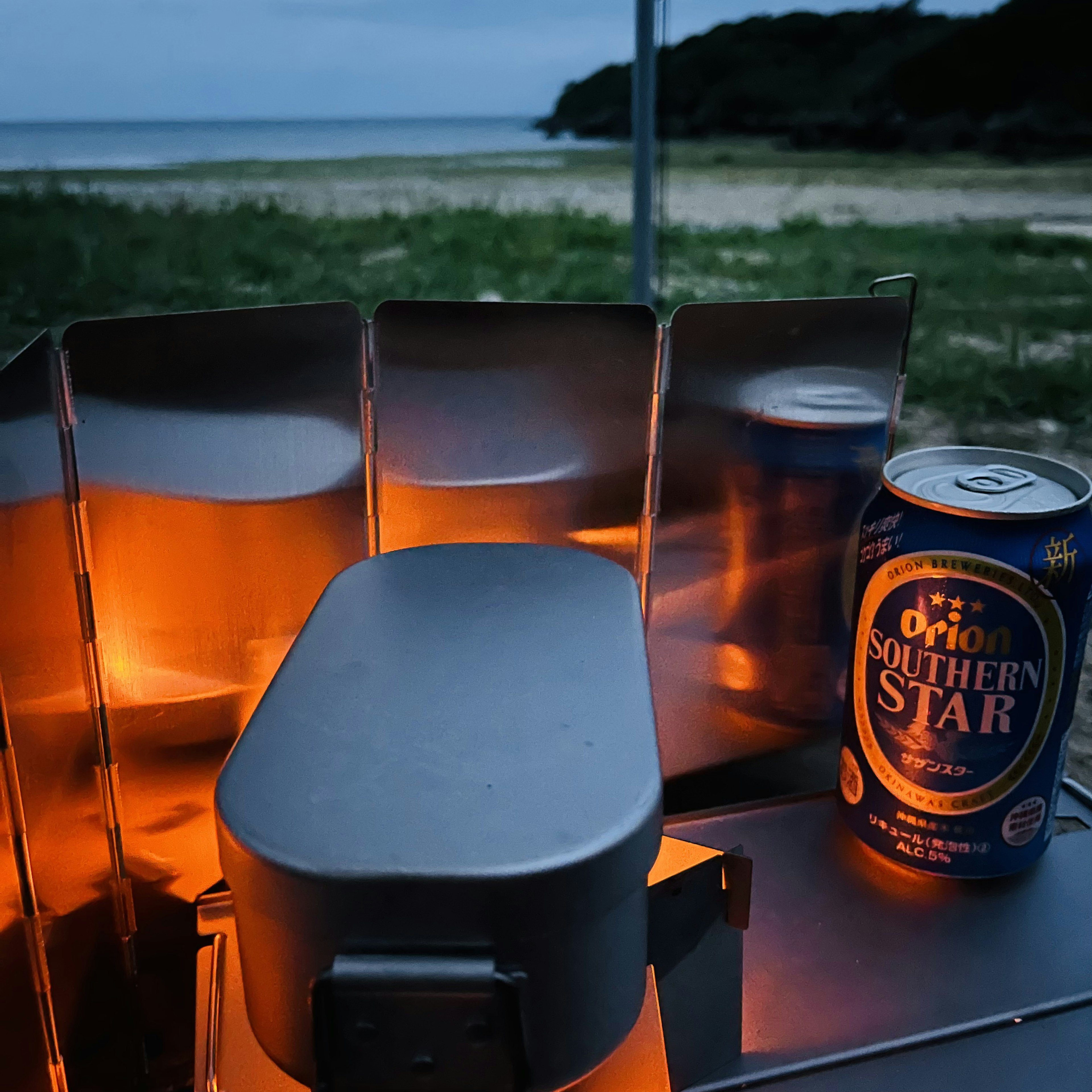 夕暮れの海辺で光るキャンプストーブと飲み物