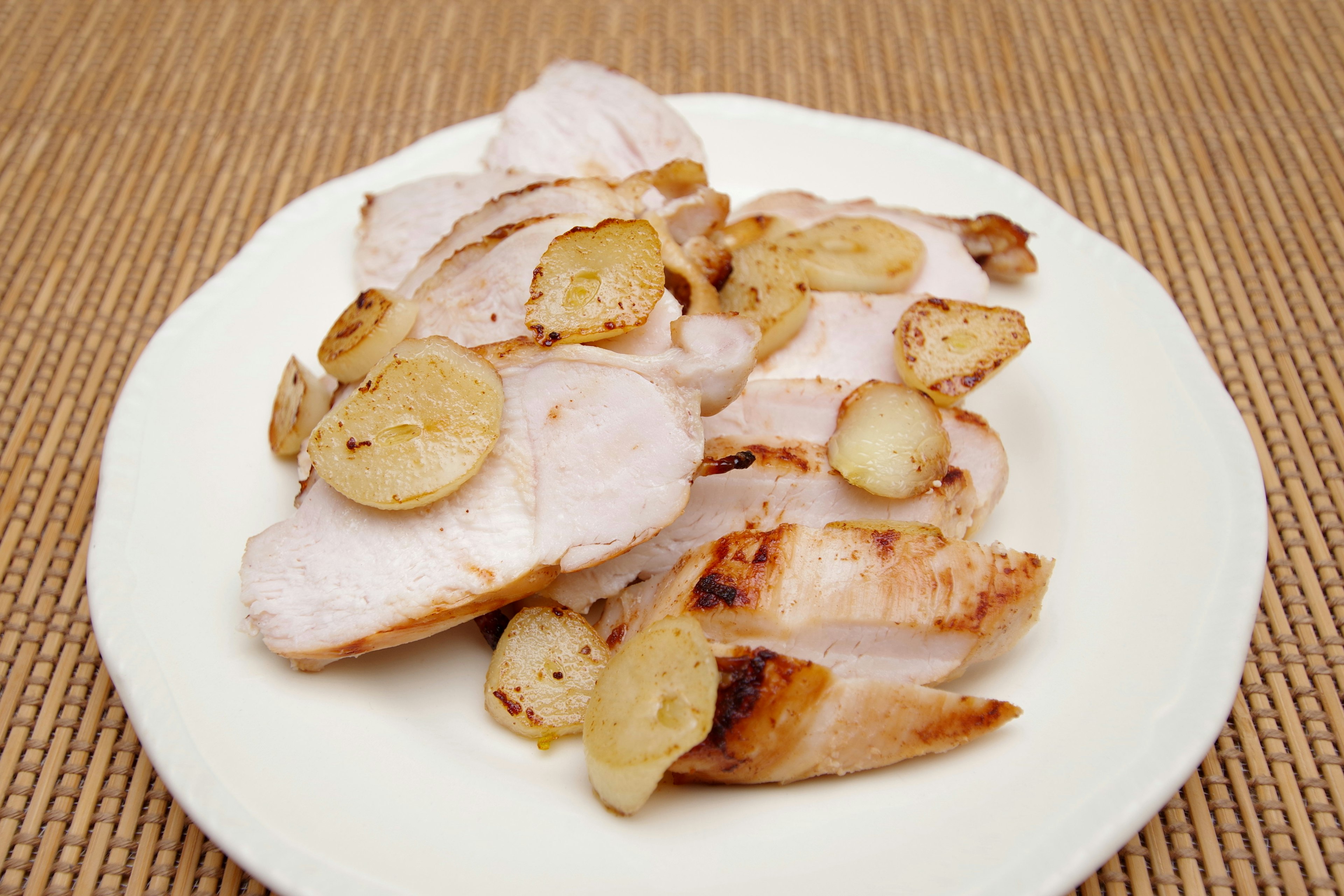 Pollo a la parrilla en rodajas servido con rodajas de ajo en un plato blanco