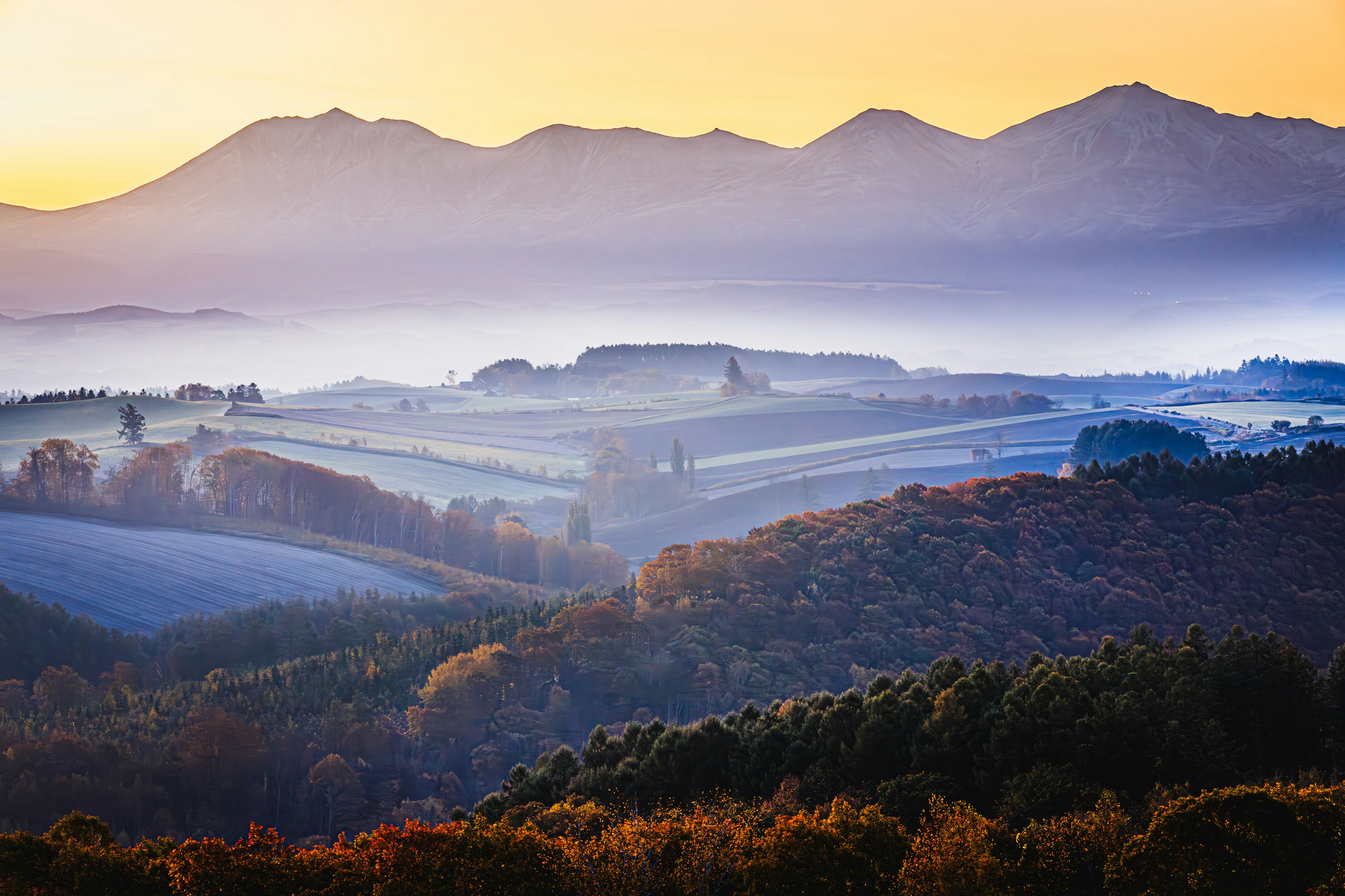 Nebelige Berge mit weitläufigen landwirtschaftlichen Flächen unter schönem Morgenlicht