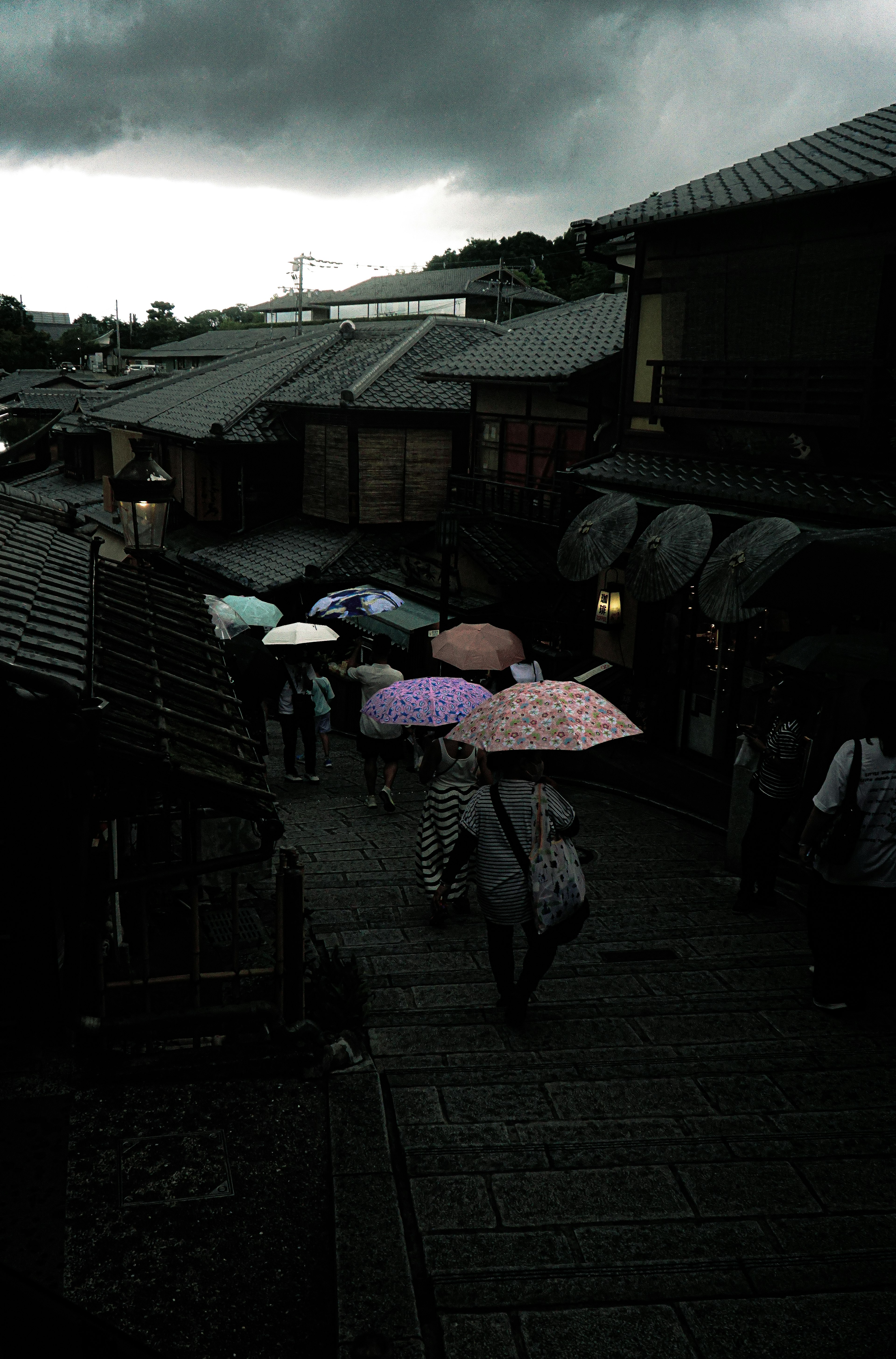 暗い雲の下で傘を持った人々が歩く古い街並みの風景